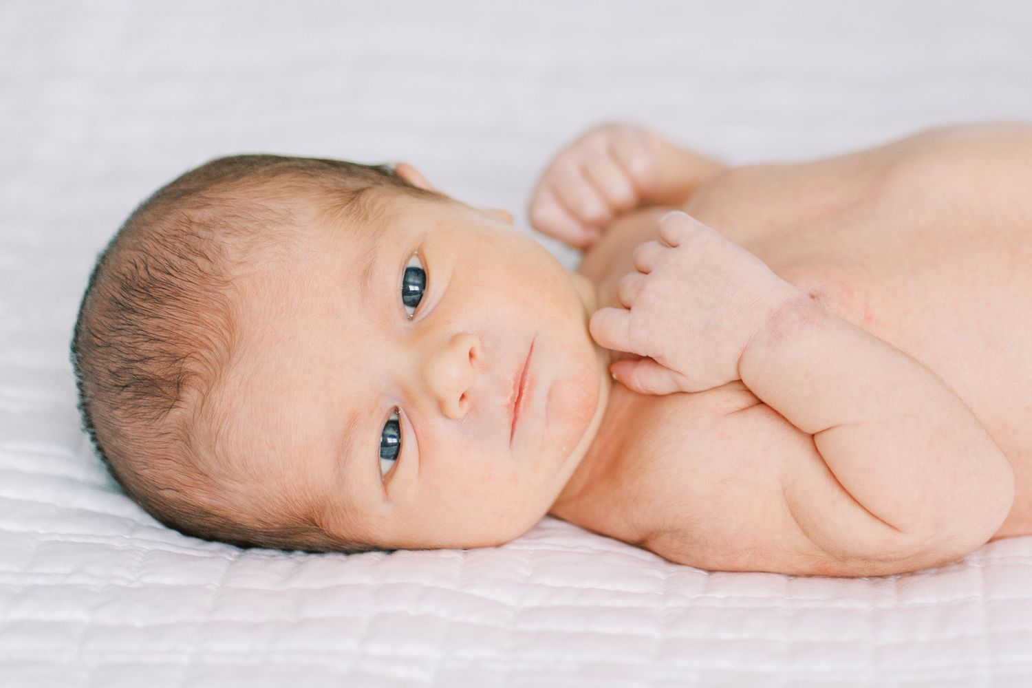 A newborn baby lying on white blankets in a series of artistic profile portraits.