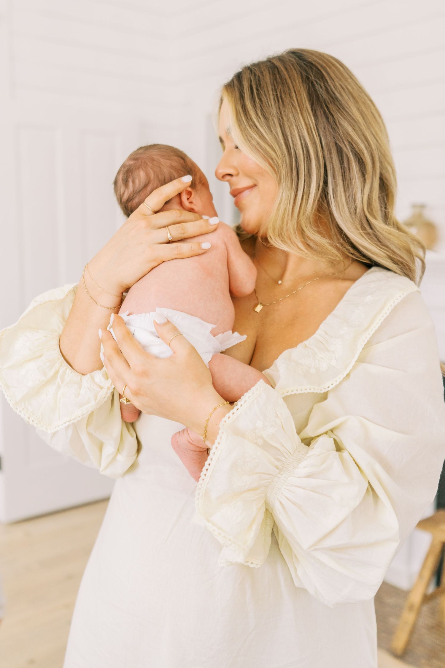 Woman in cream dress holds newborn baby in tender embrace.