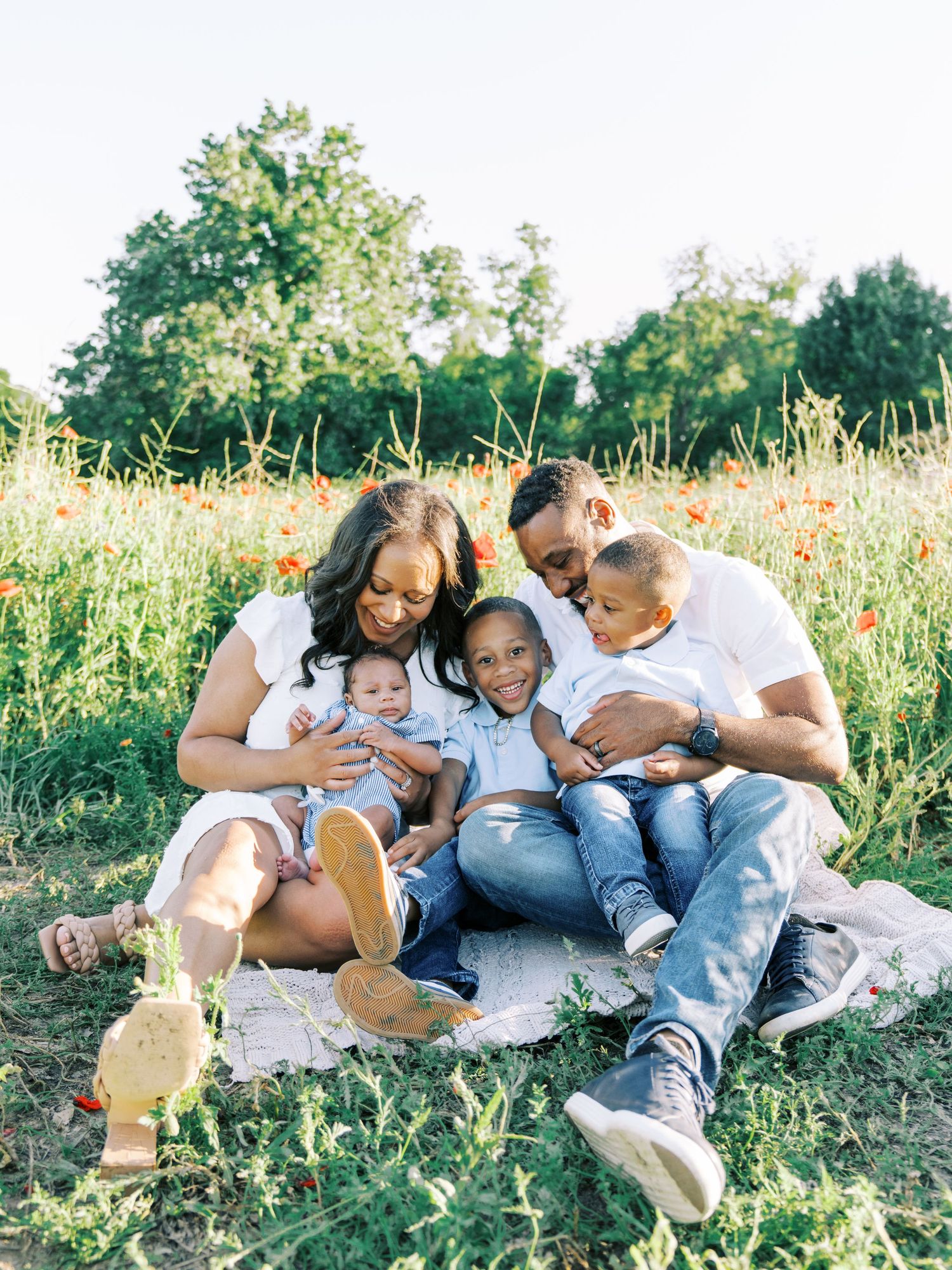 A joyful family of five sits together in a vibrant poppy field, sharing a loving moment outdoors.
