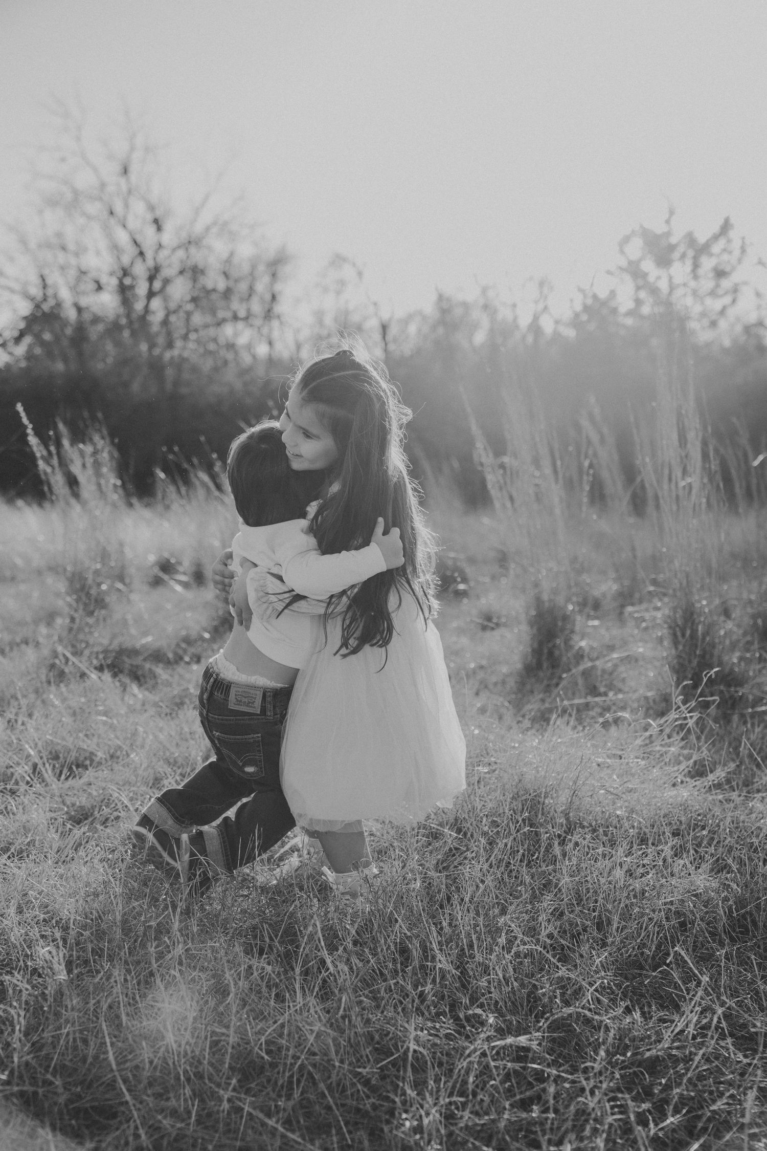 Black and white photo captures loving embrace in tall grass field.