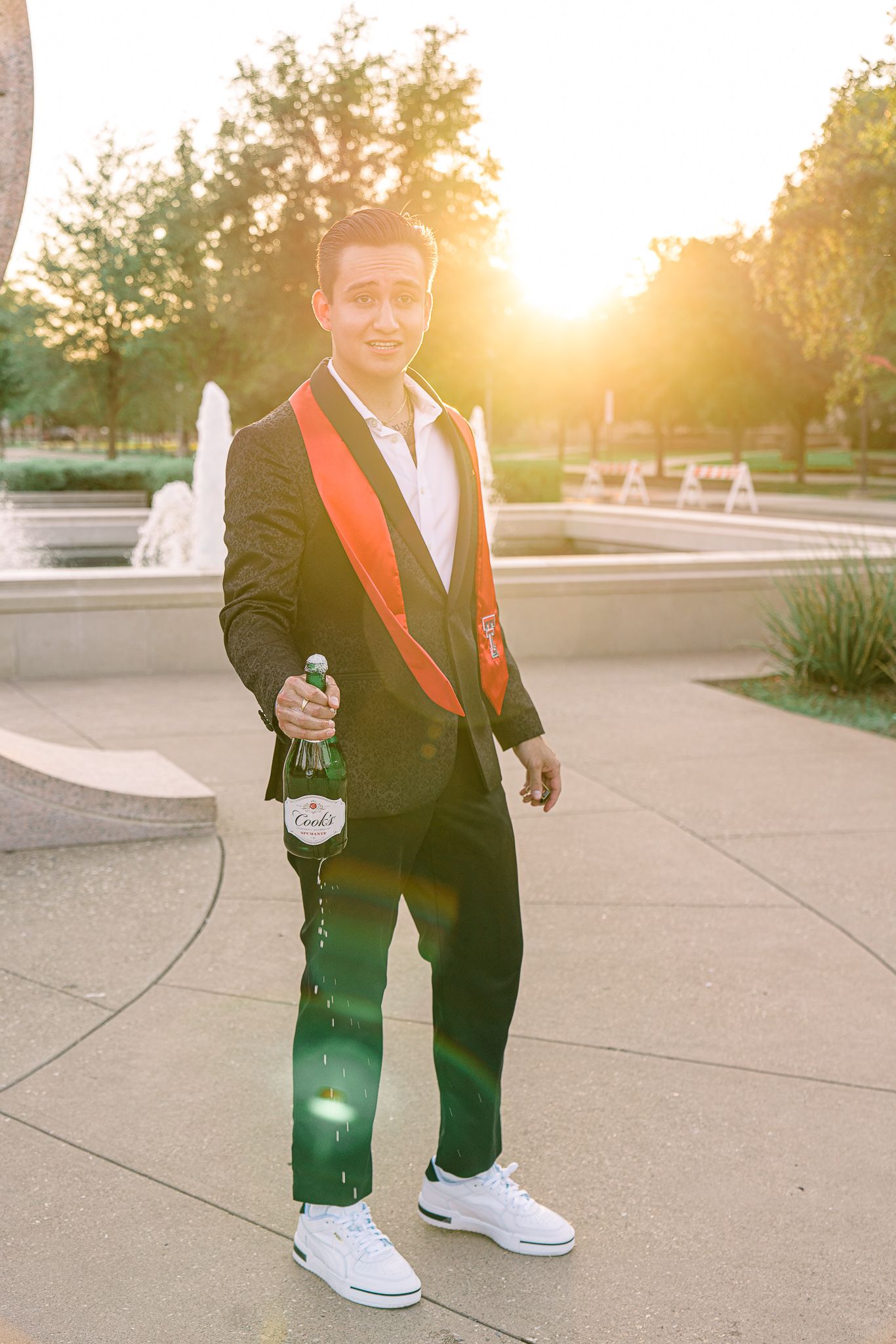 Person in black suit with red accents and white sneakers poses at sunset in an outdoor setting.