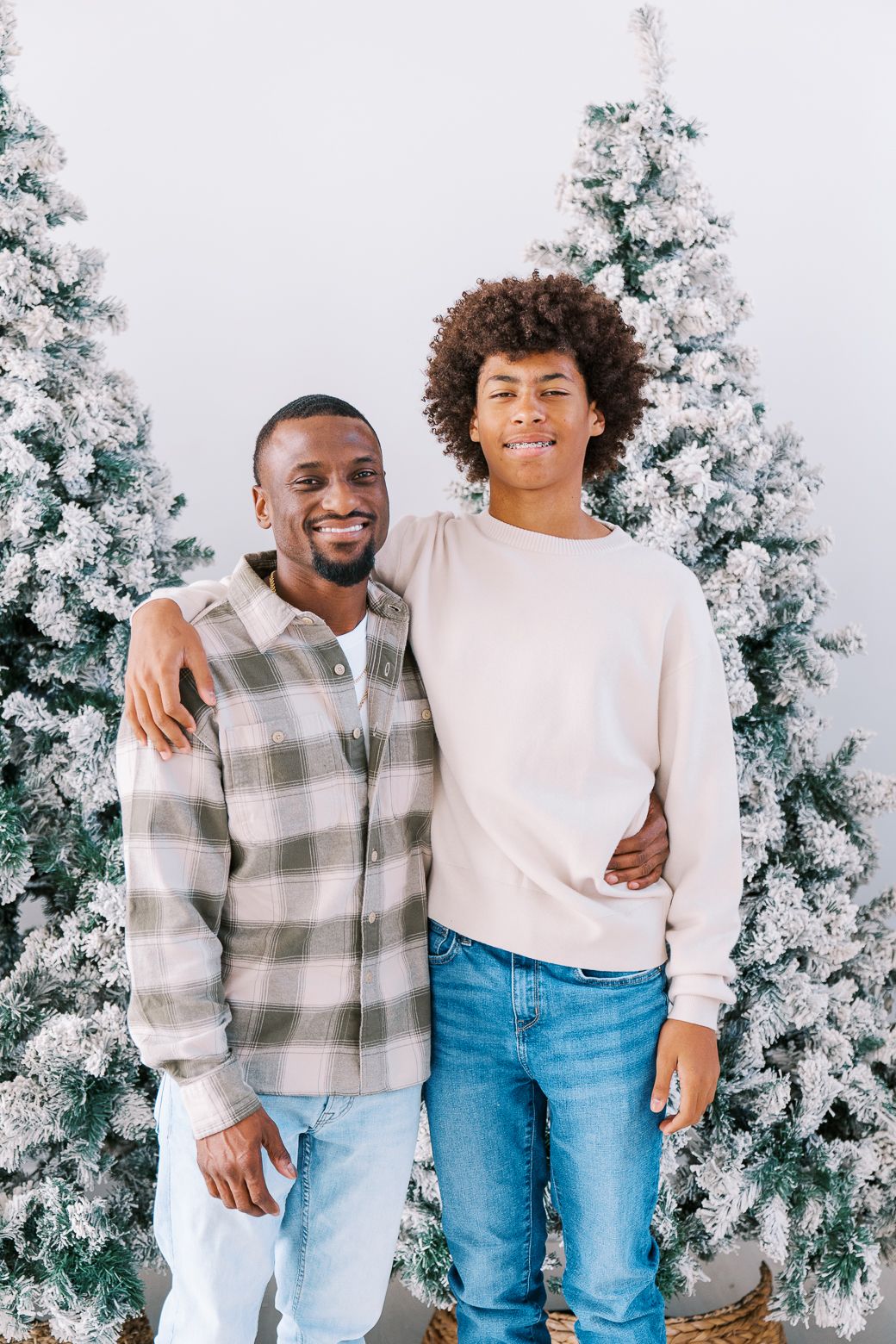 Casual holiday portrait session with family members in coordinating outfits against snowy Christmas trees.