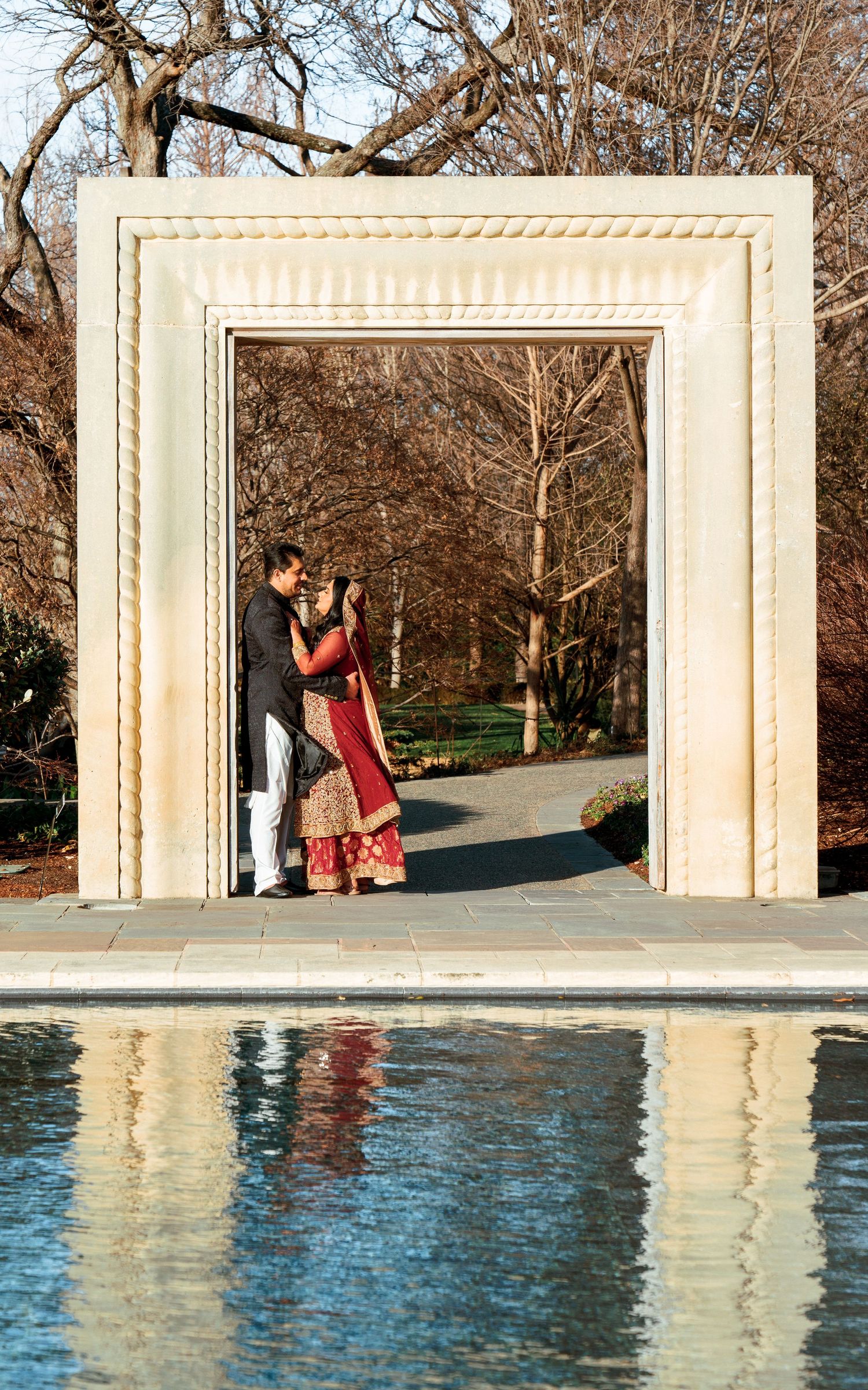 A couple poses in an elegant archway setting with a reflecting pool during their wedding photoshoot.