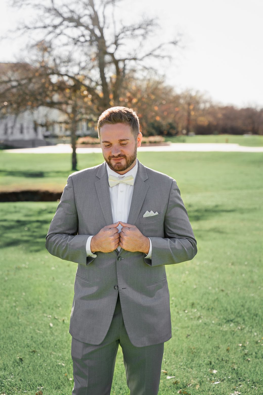 A person in a gray suit enjoys eating a sandwich outdoors on a grassy lawn during autumn.