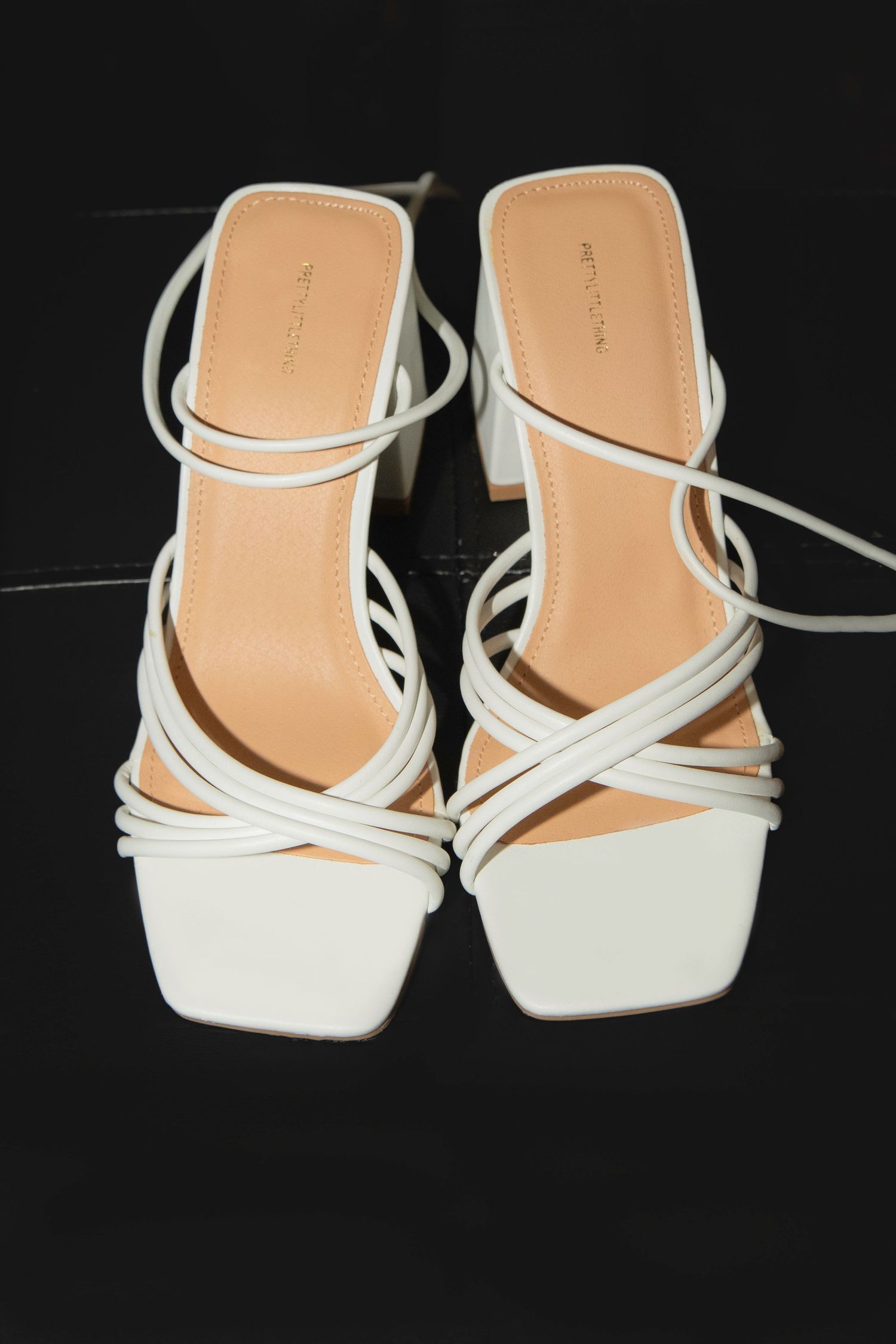 Elegant white strappy sandals with thin crossing straps and kitten heels photographed against a black background.