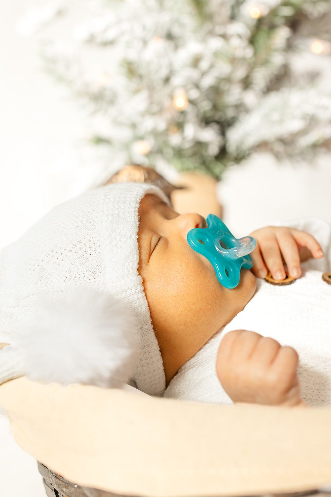 Sleeping baby with turquoise pacifier wearing white clothing in soft focus.