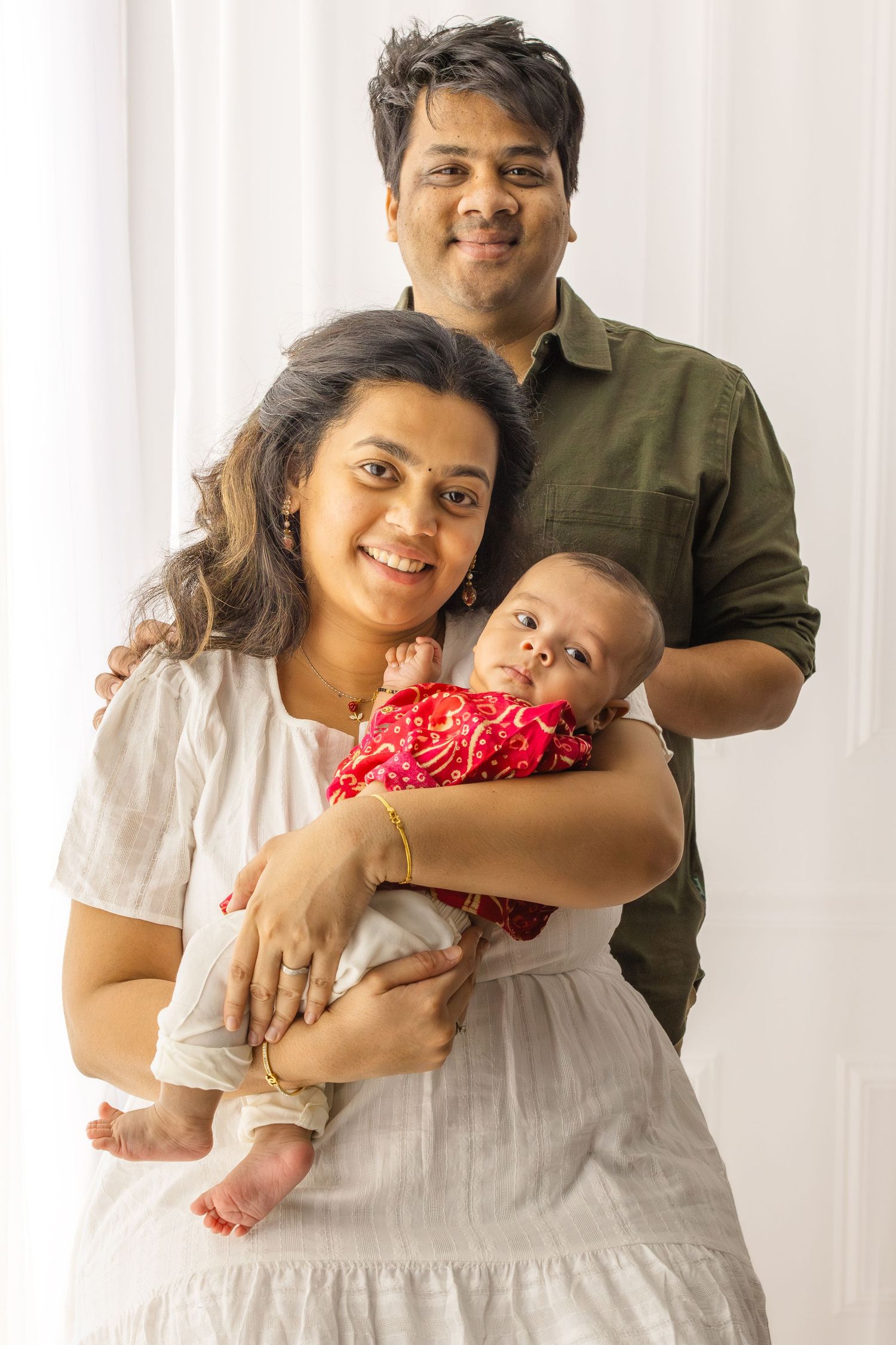 A family portrait with a baby wearing a red outfit against a white background.