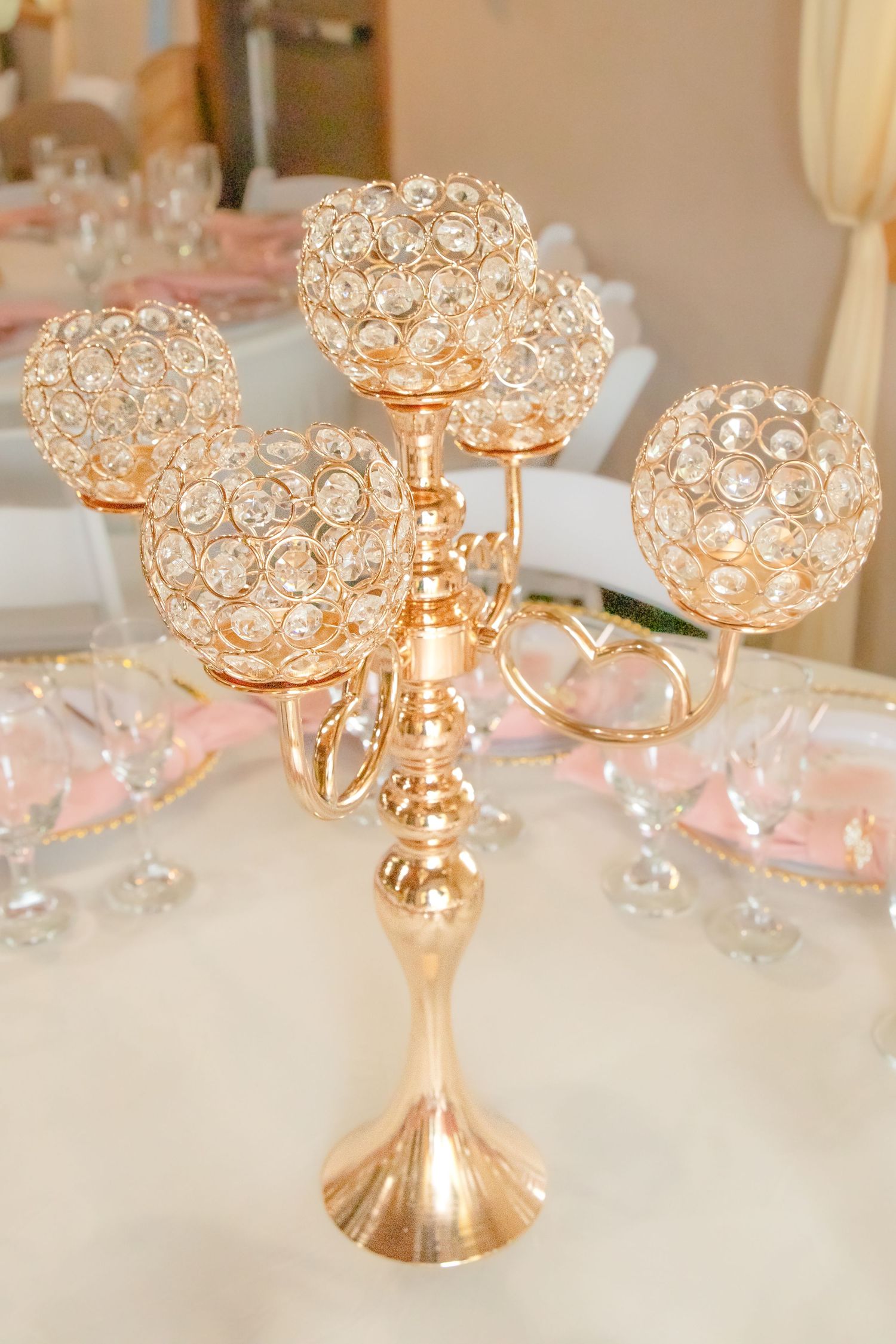 Gold crystal candle holders with beaded details arranged on white tablecloth at wedding reception.