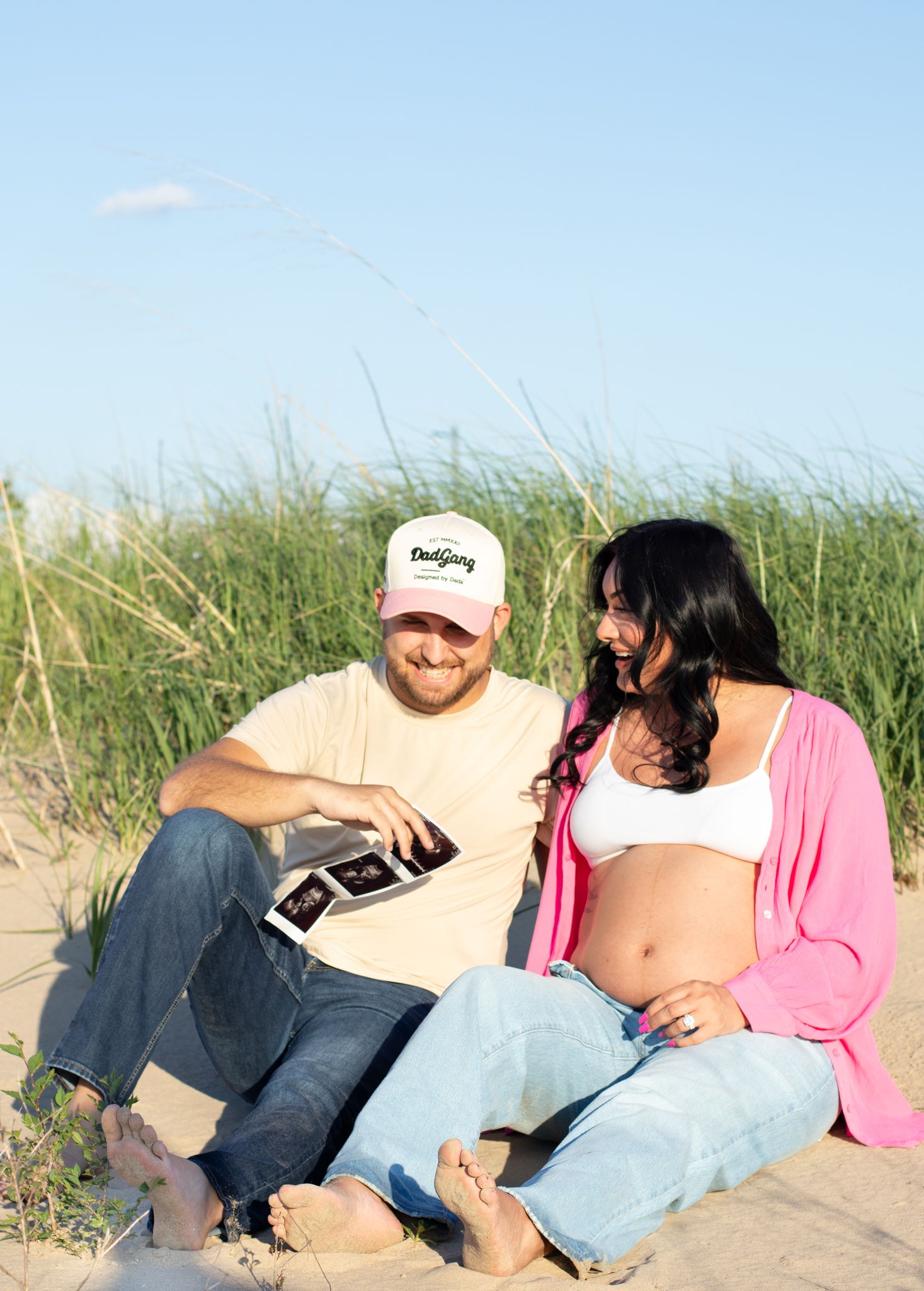 Couple looking at ultrasound photos while sitting in beach grass during maternity shoot.