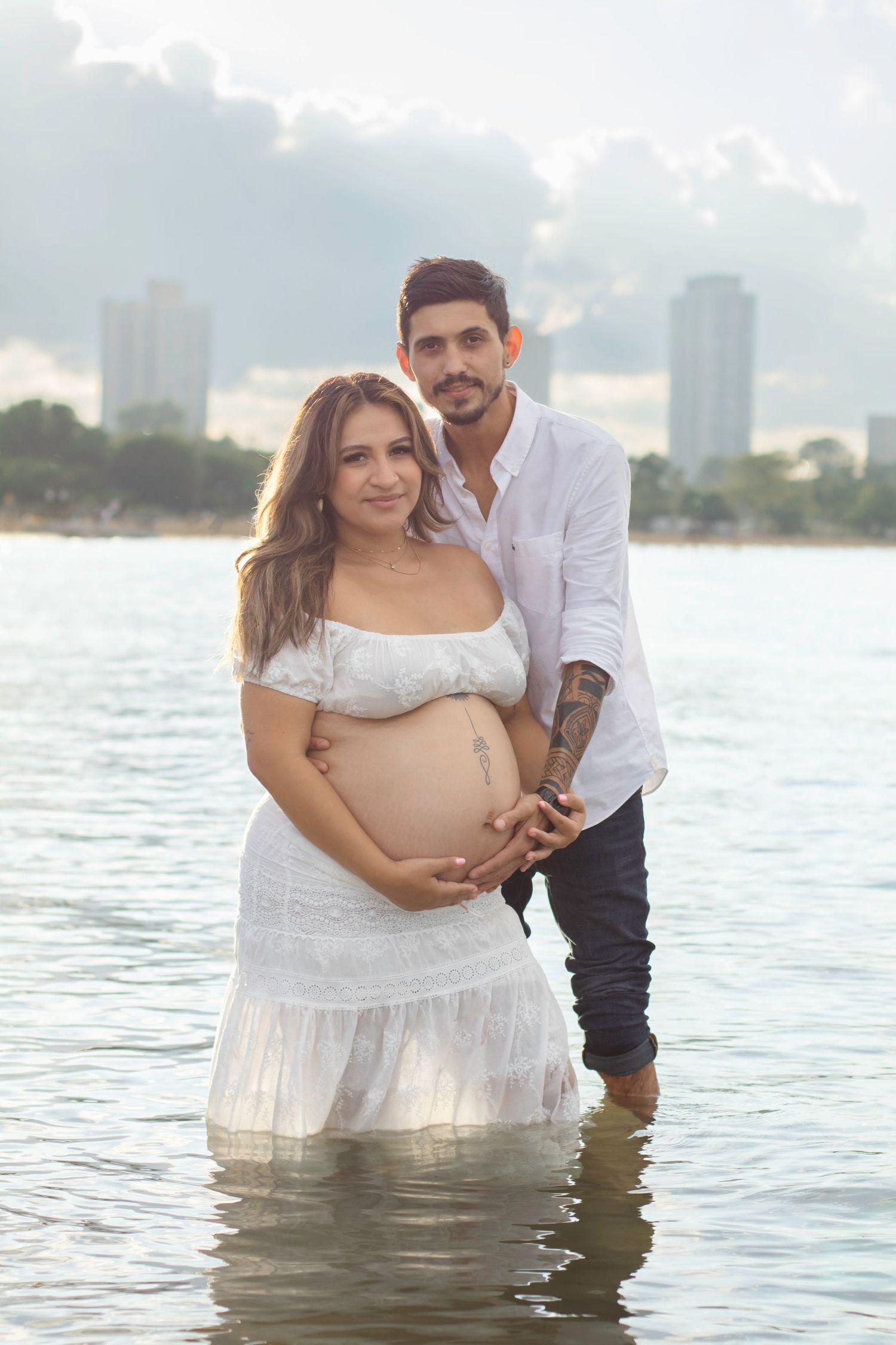 Maternity photoshoot with couple standing in Lake Michigan water at sunset.