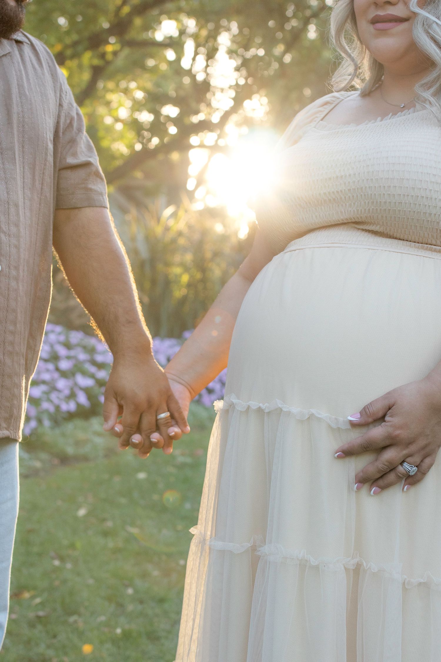 Close-up view of hands resting on a white dress during an outdoor sunset photoshoot.