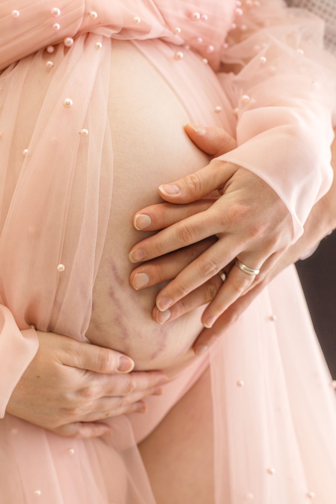 Close-up series of hands tenderly cradling baby bump through delicate pink pearl-studded fabric.