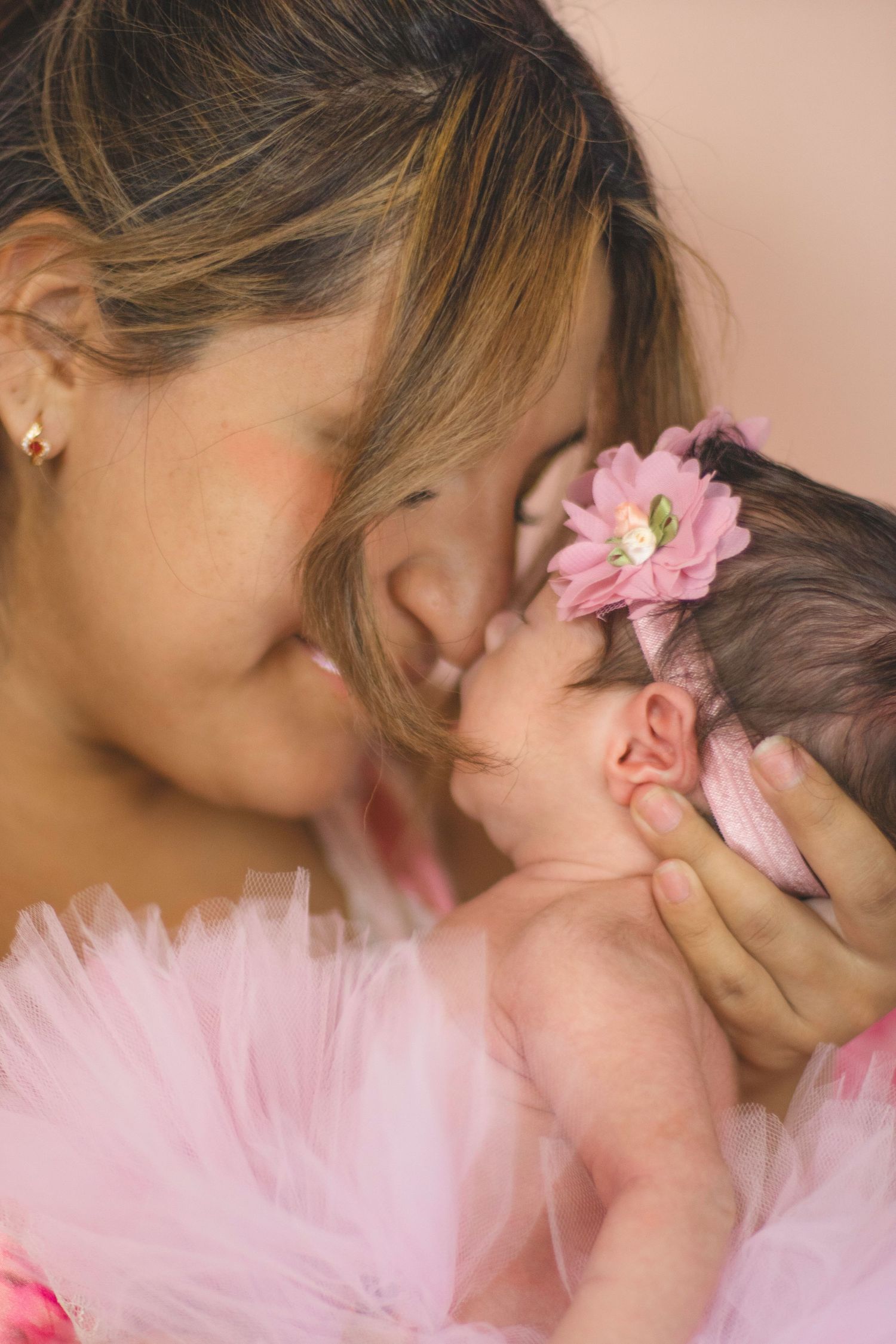 Tender moment between mother and newborn baby with pink flower accent.