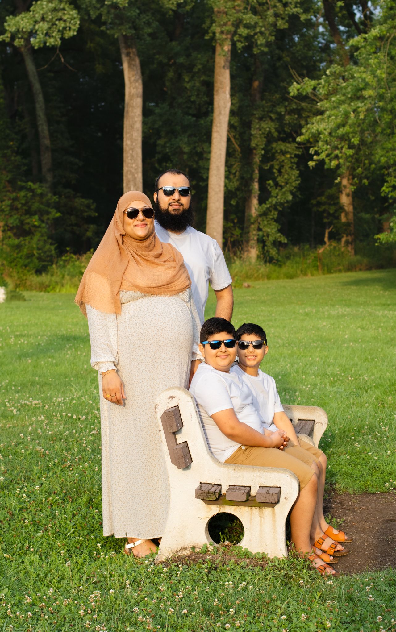 Family takes portrait on concrete bench in wooded park setting during summer.