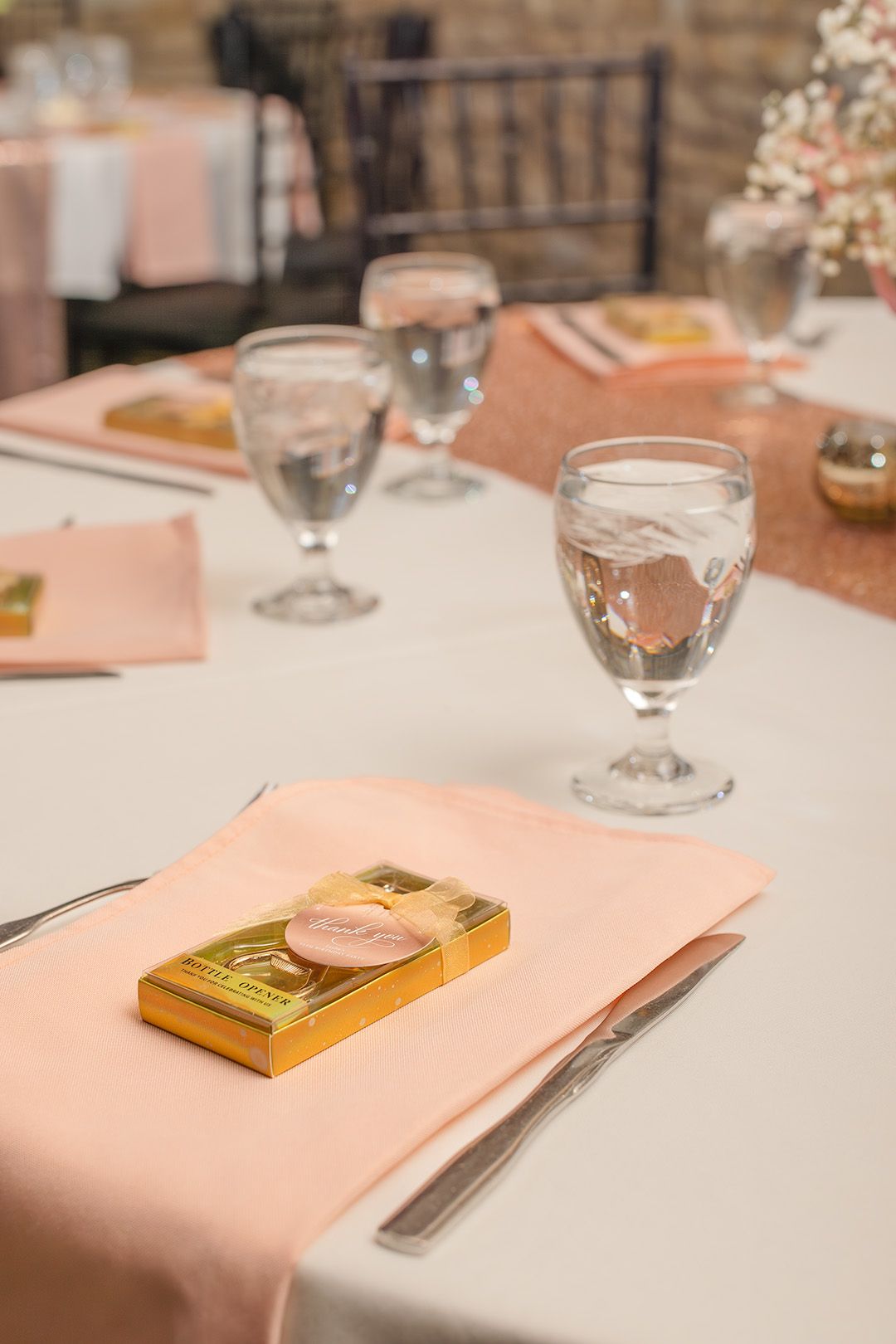 Elegant wedding reception table setting with blush pink napkins, crystal glasses, and gold Lindt chocolate favors.