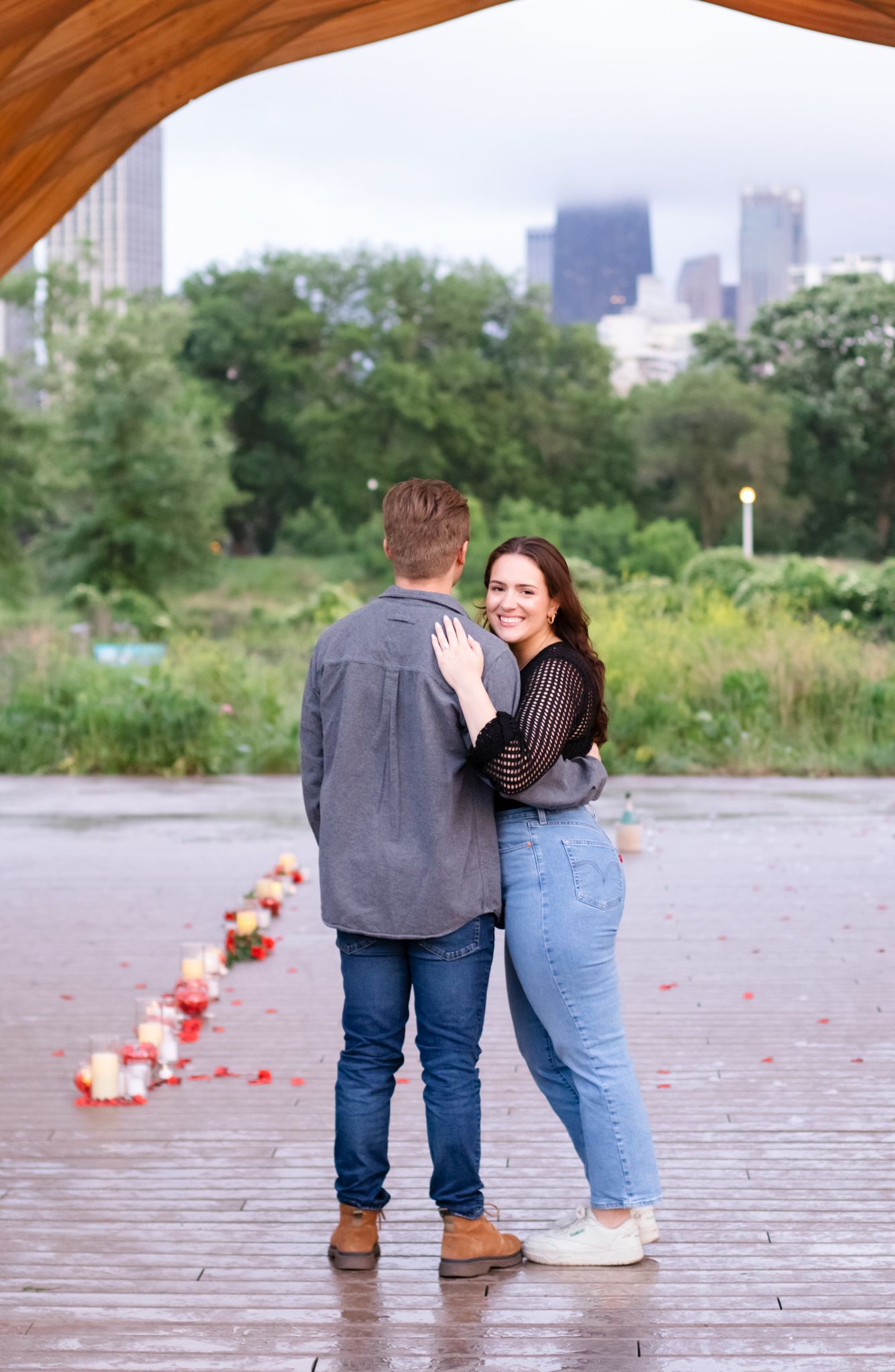 A couple shares a romantic moment on a wooden deck with candles and city buildings visible in the background.
