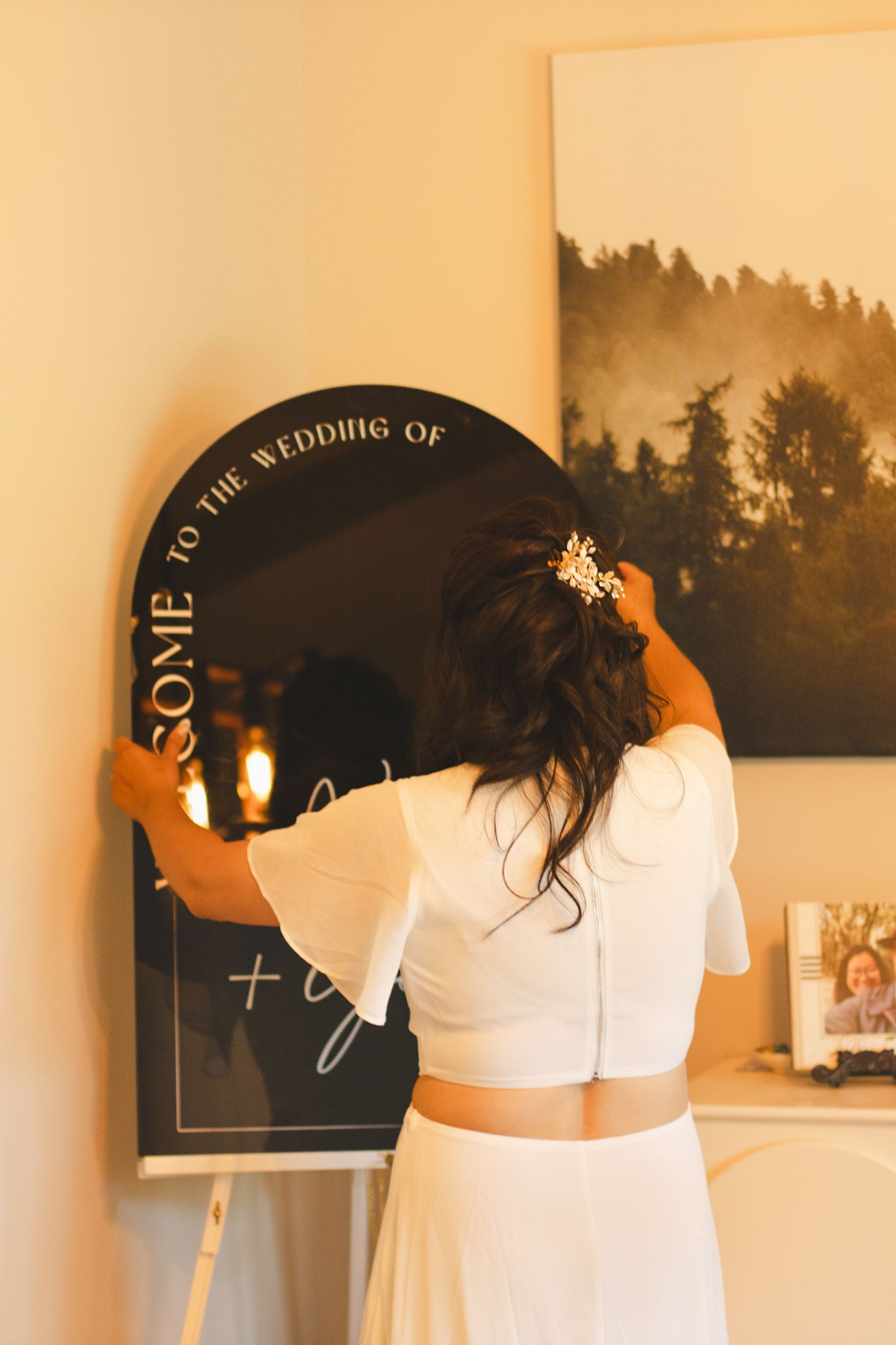 Someone writing on black round welcome sign with forest backdrop artwork.