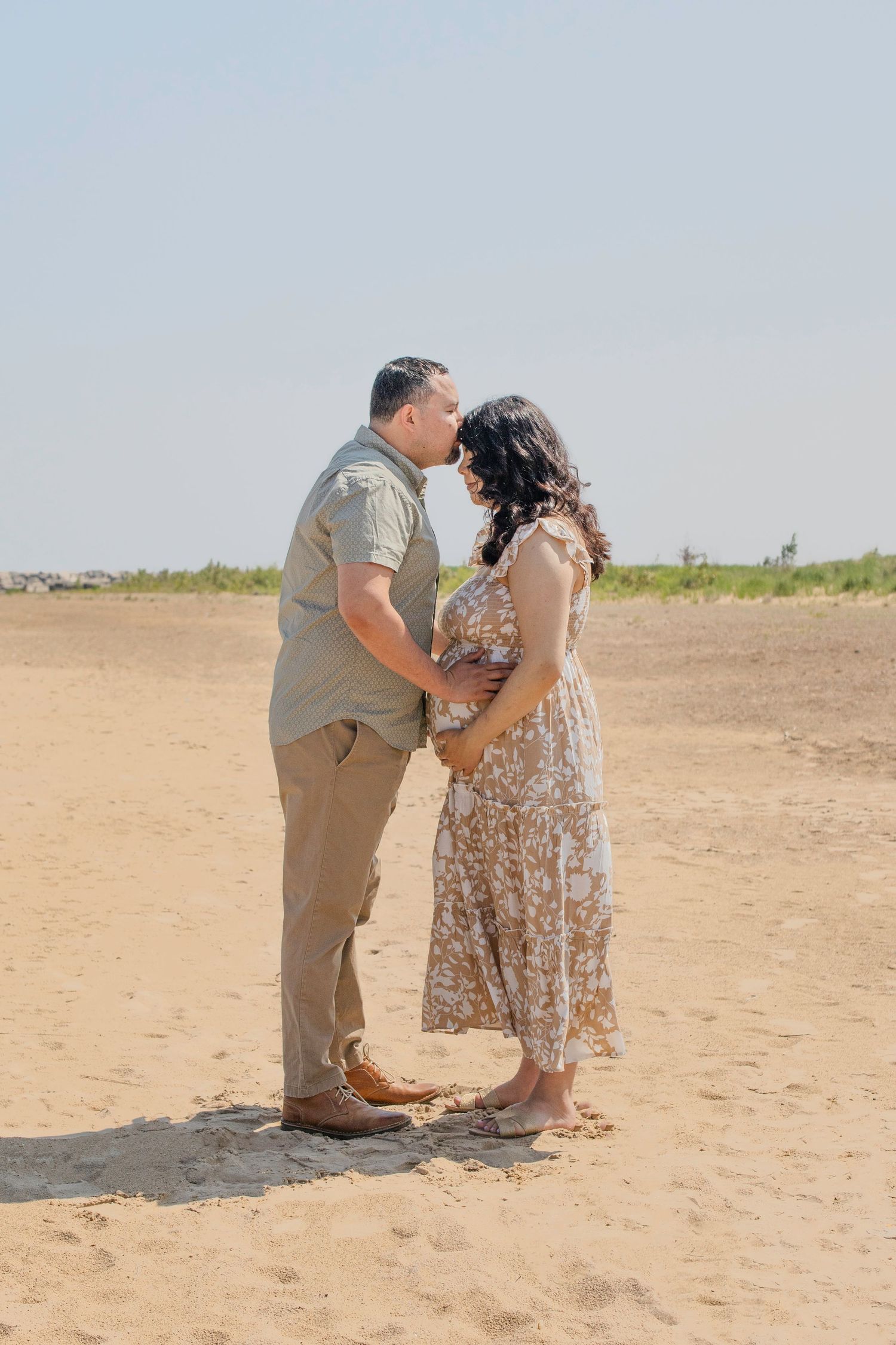A couple shares a tender moment during their beach proposal as they kneel together on the sandy shore.