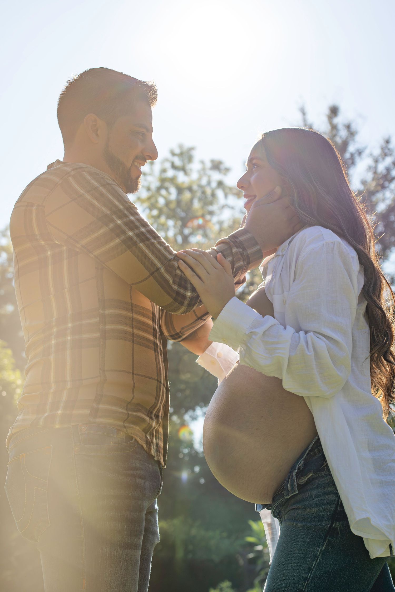 A romantic couple embraces and dances together outdoors in warm sunlight with trees visible in the background.