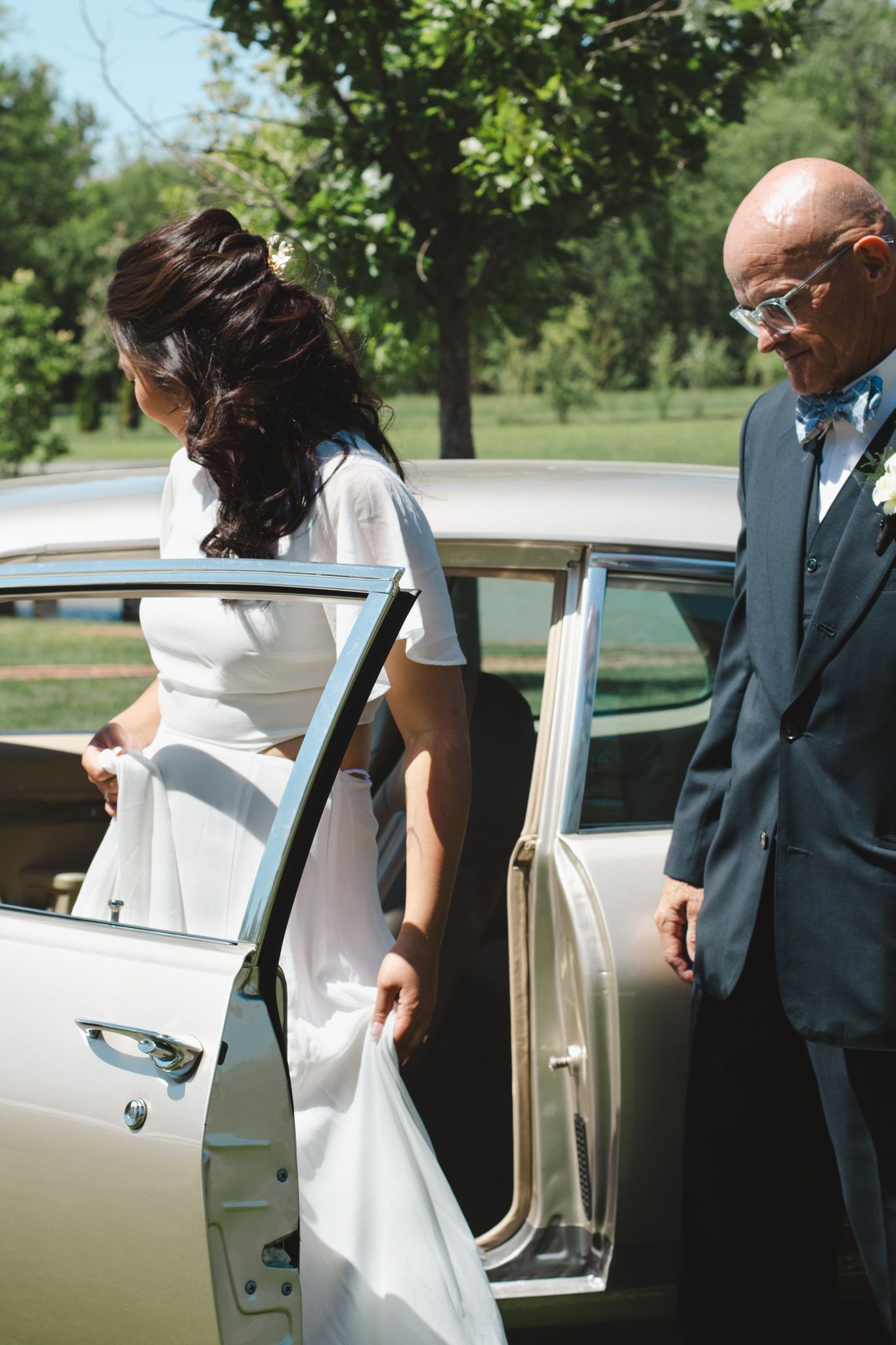 Classic white car door being opened for someone wearing formal attire at outdoor celebration.
