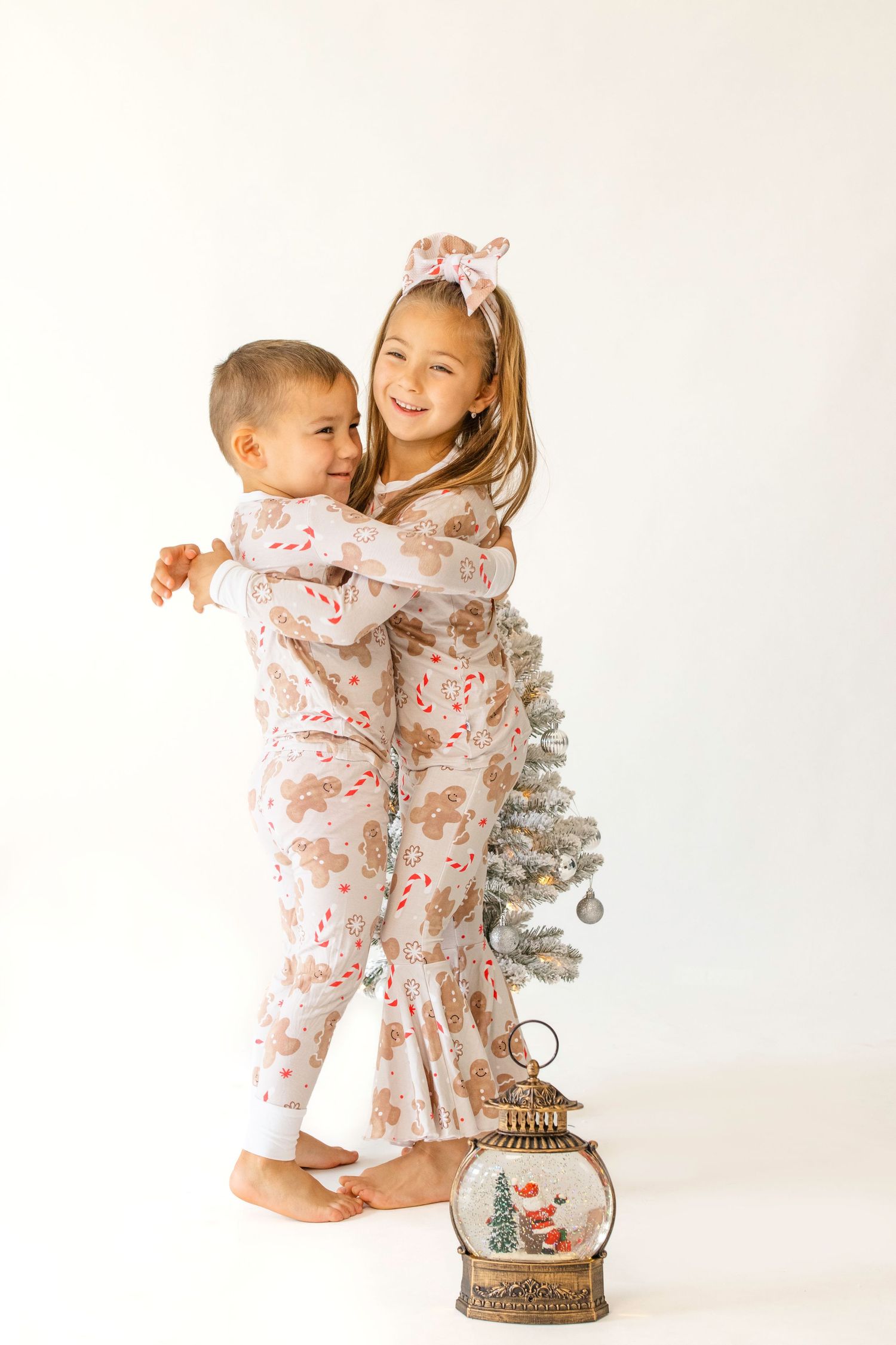 Children in matching floral outfits play near a small decorative Christmas tree and vintage lantern.