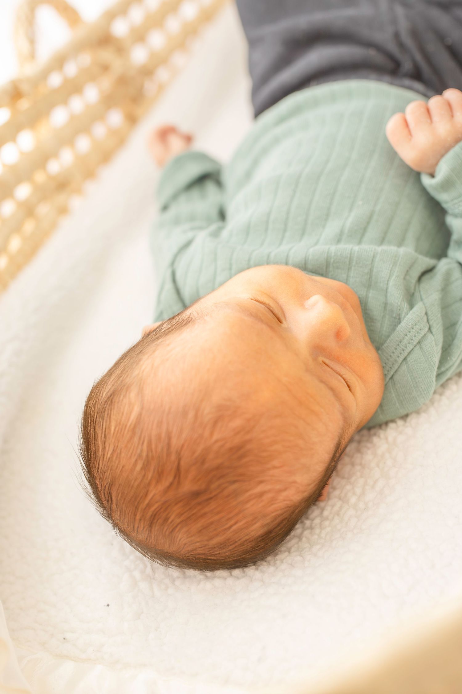 Side view of a sleeping baby in a mint green outfit lying on a white blanket.