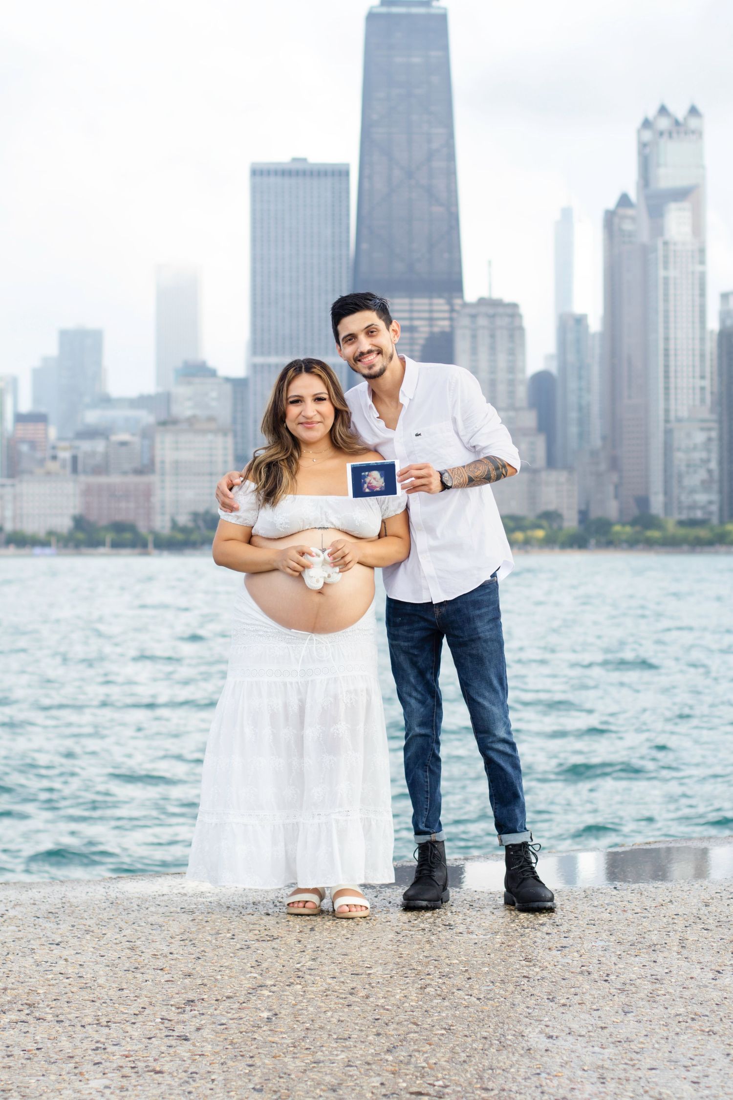 Expectant couple poses with ultrasound photo against Chicago skyline backdrop.