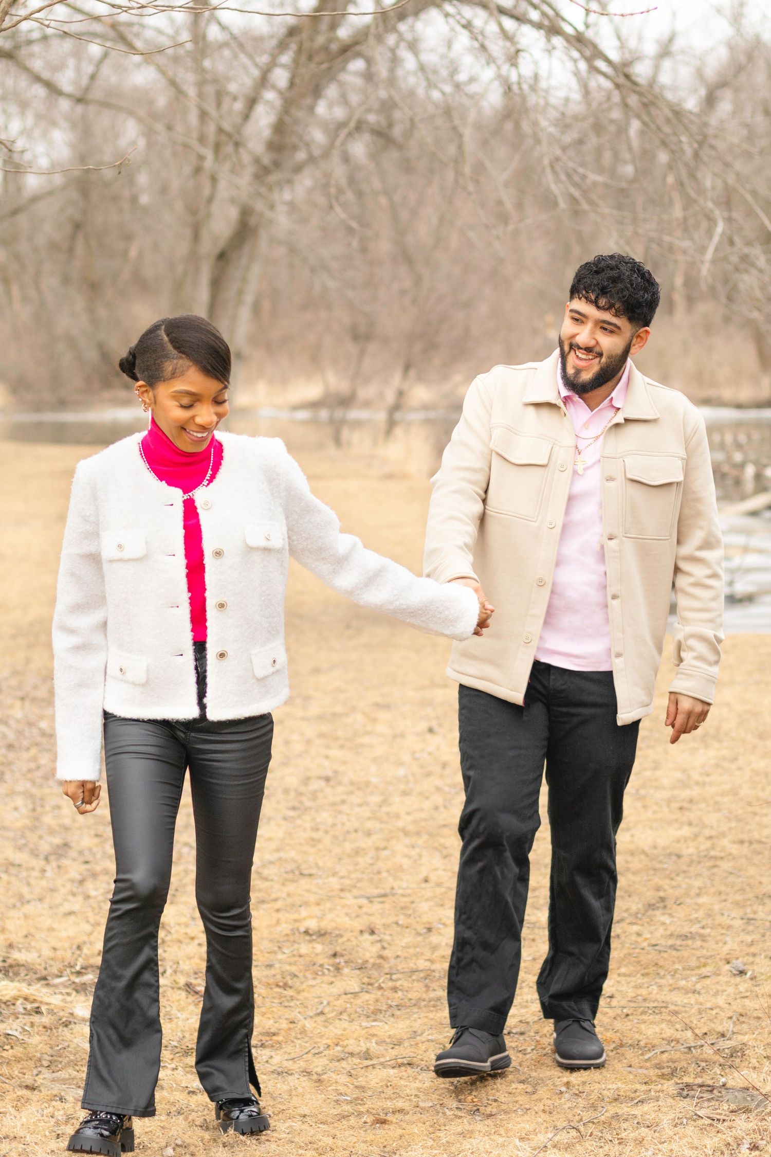 A couple walks together on a path through bare winter trees wearing coordinated outfits.
