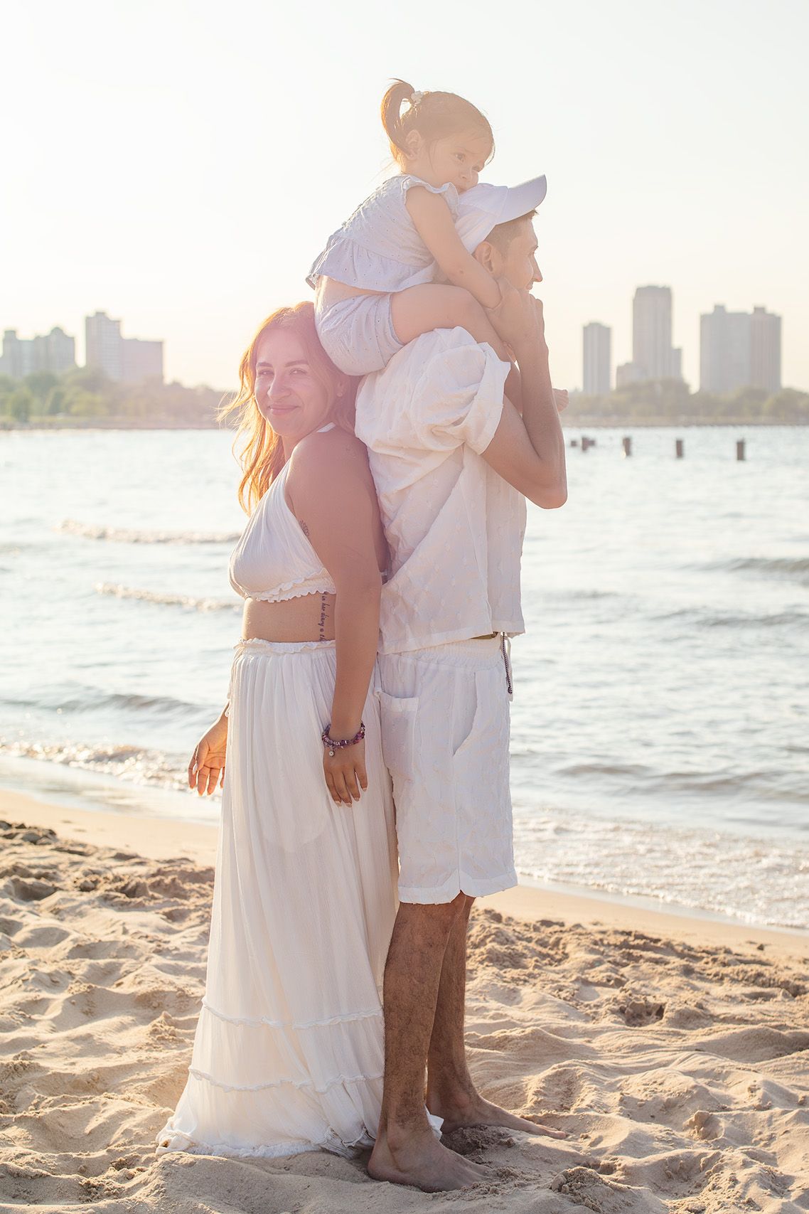 Happy family in white outfits posing on a sunny beach with city skyline.
