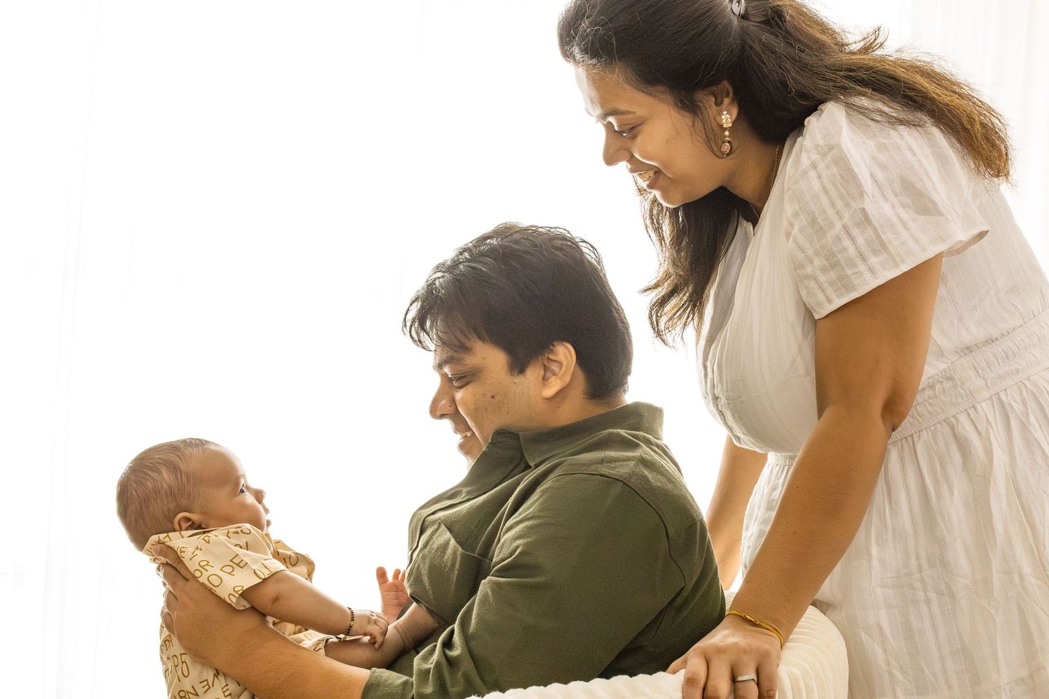 Parents share tender moments with their baby while sitting near a sunlit window.