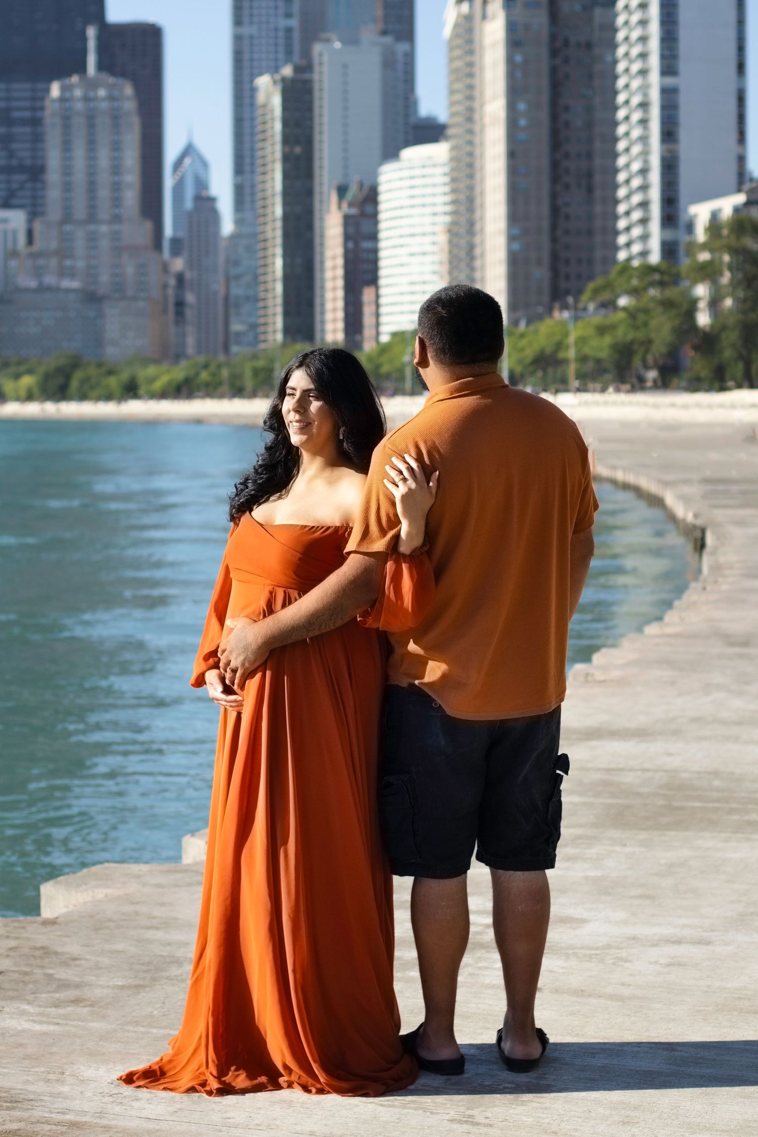 Couple standing on Lake Michigan shoreline with Chicago skyscrapers in background.