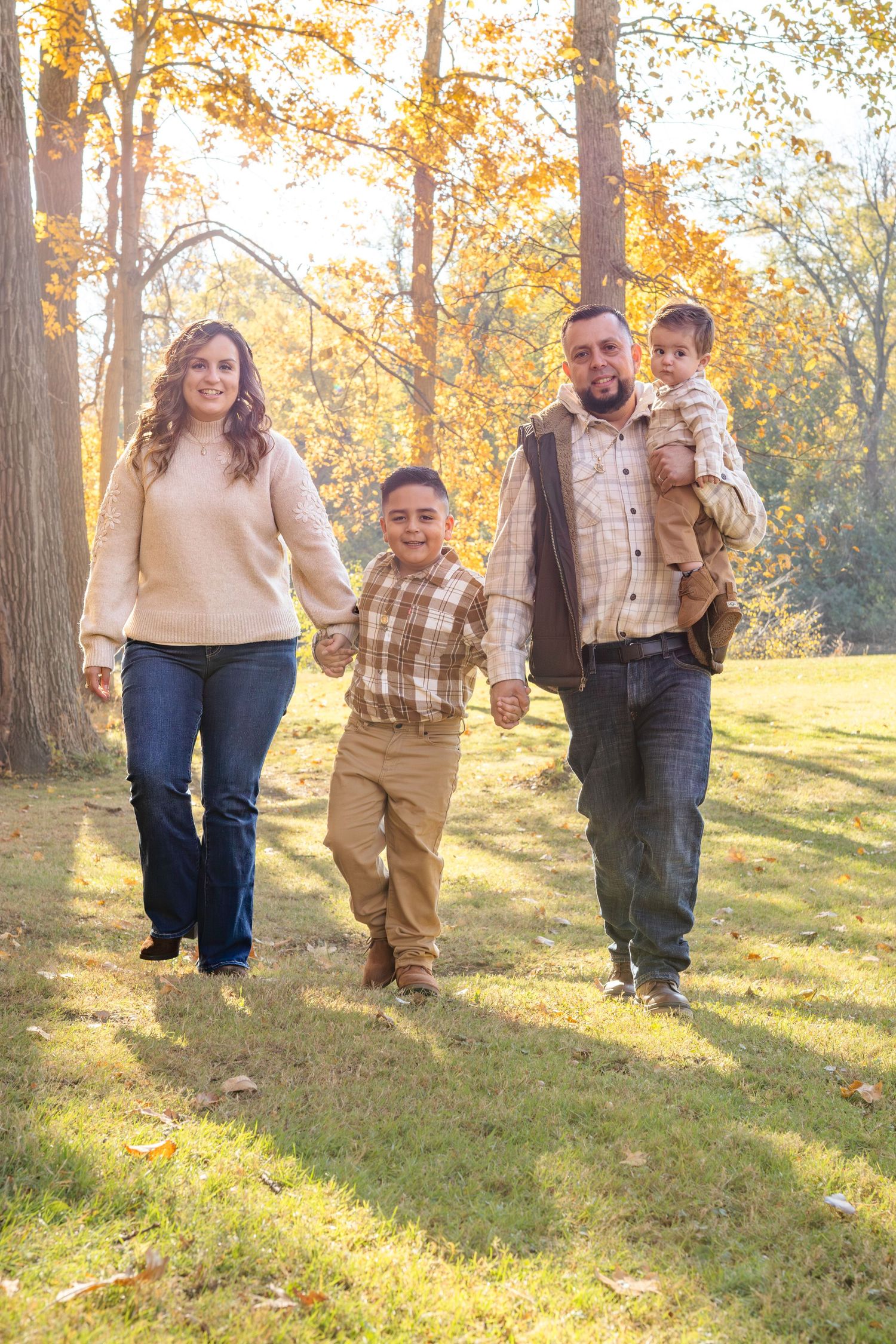 A family walks together through a sunlit autumn forest with golden leaves and dappled light filtering through the trees.