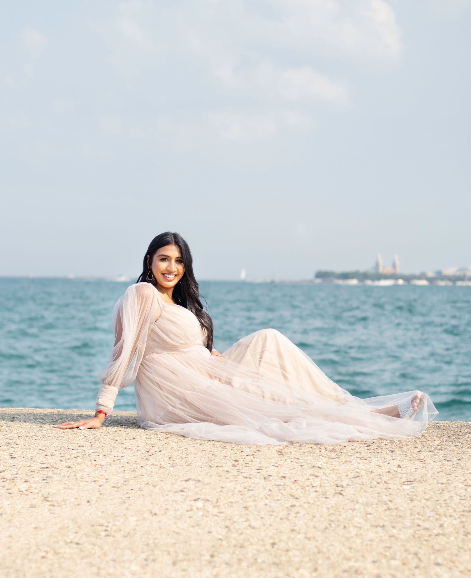 Maternity portrait on beach with turquoise waters and sailboats in background.