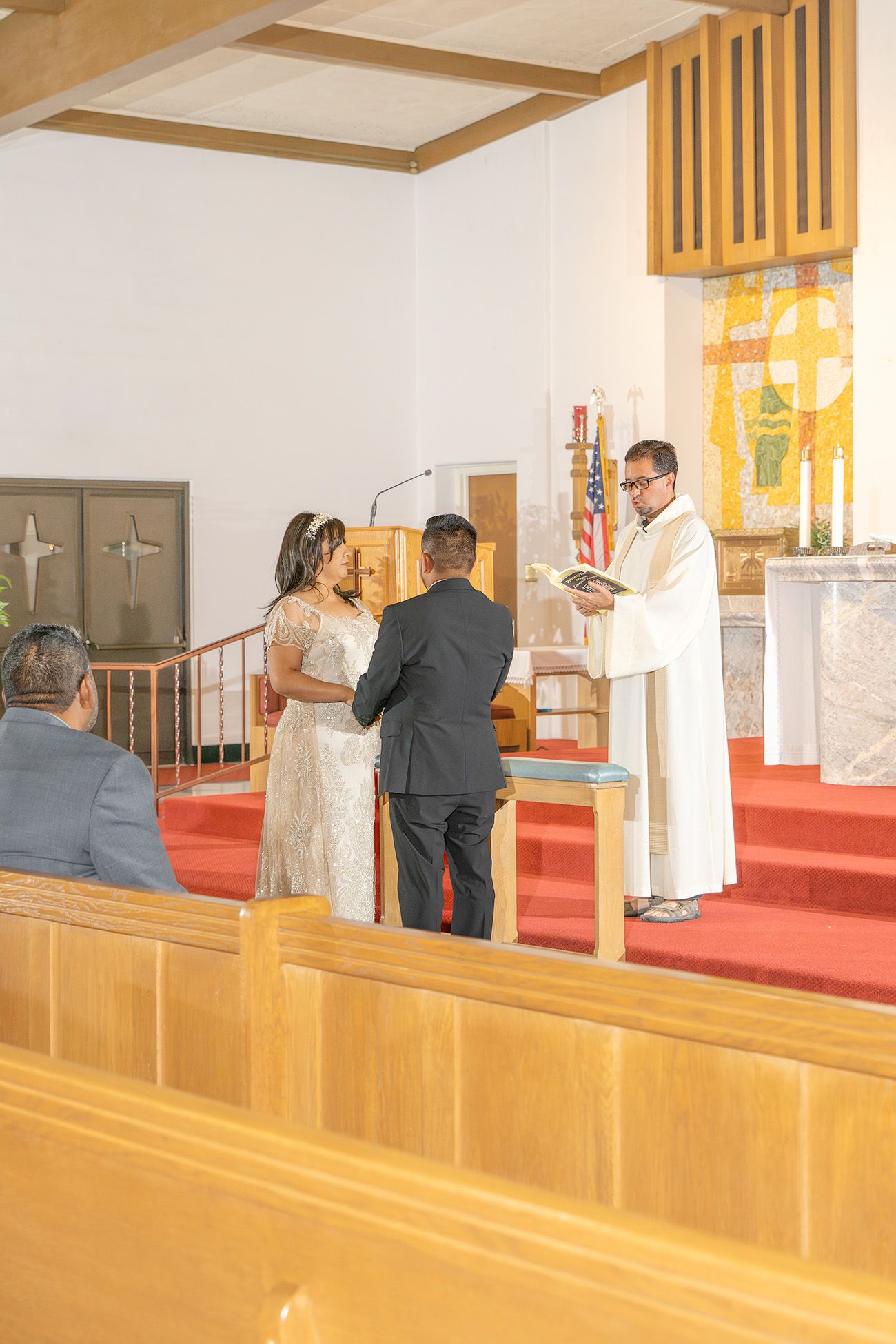 Couple exchanging vows at church altar with officiant holding book during wedding ceremony.