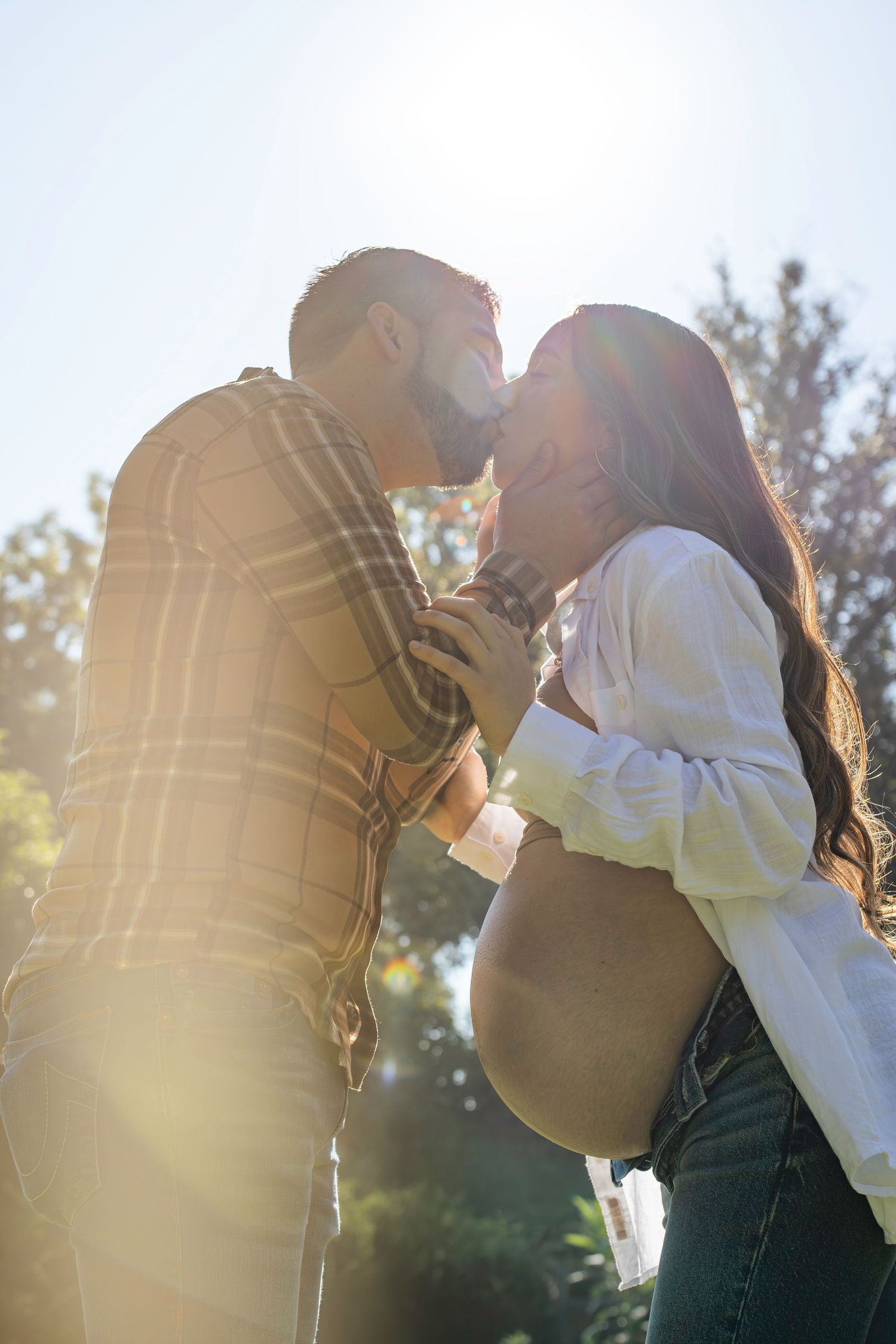 A romantic couple embraces in sunset backlit golden light, creating a soft silhouetted outdoor series of poses.