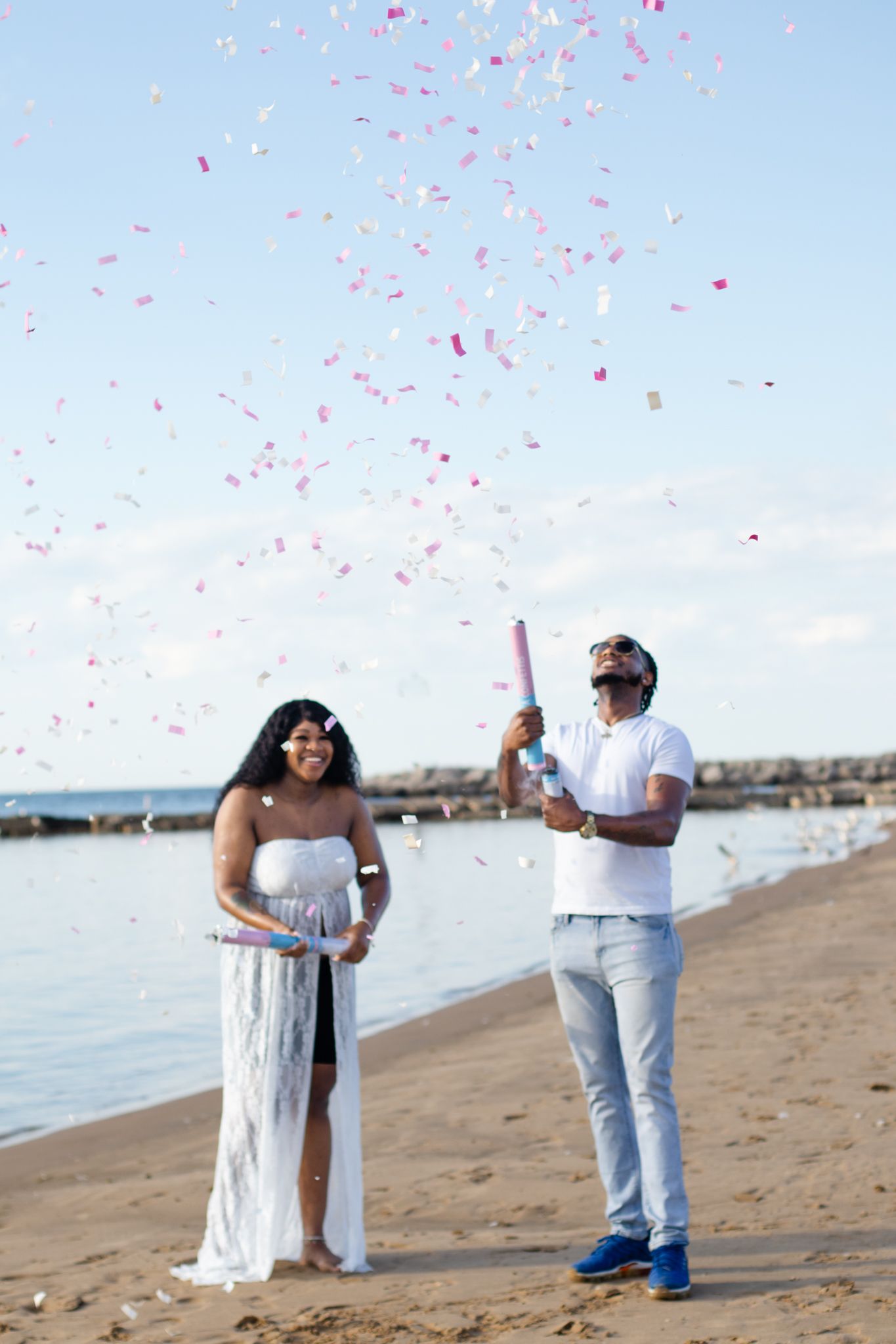 Couple celebrates on beach as pink confetti rains down during photoshoot.
