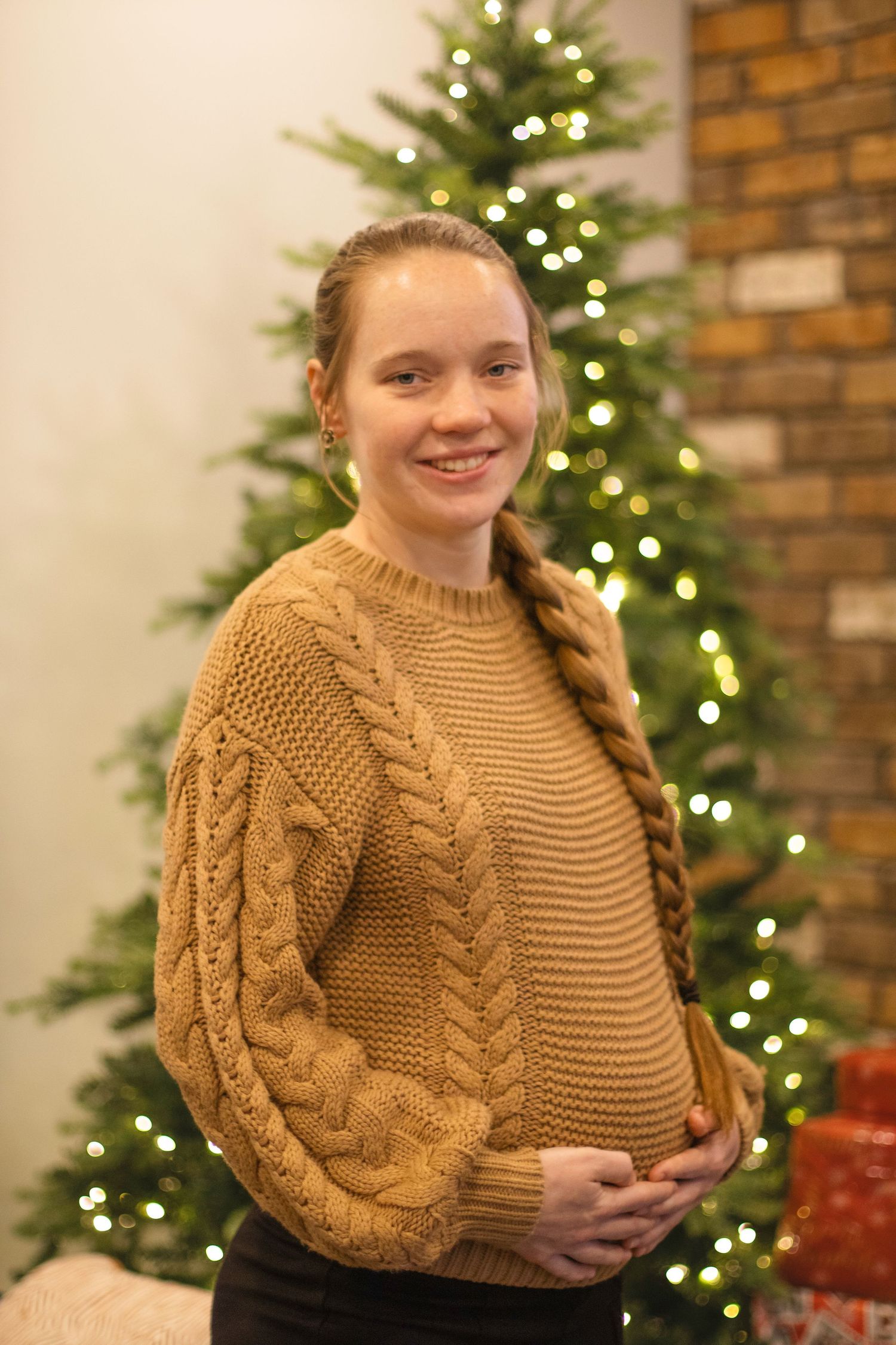 Maternity photo in front of Christmas tree wearing cable knit sweater.