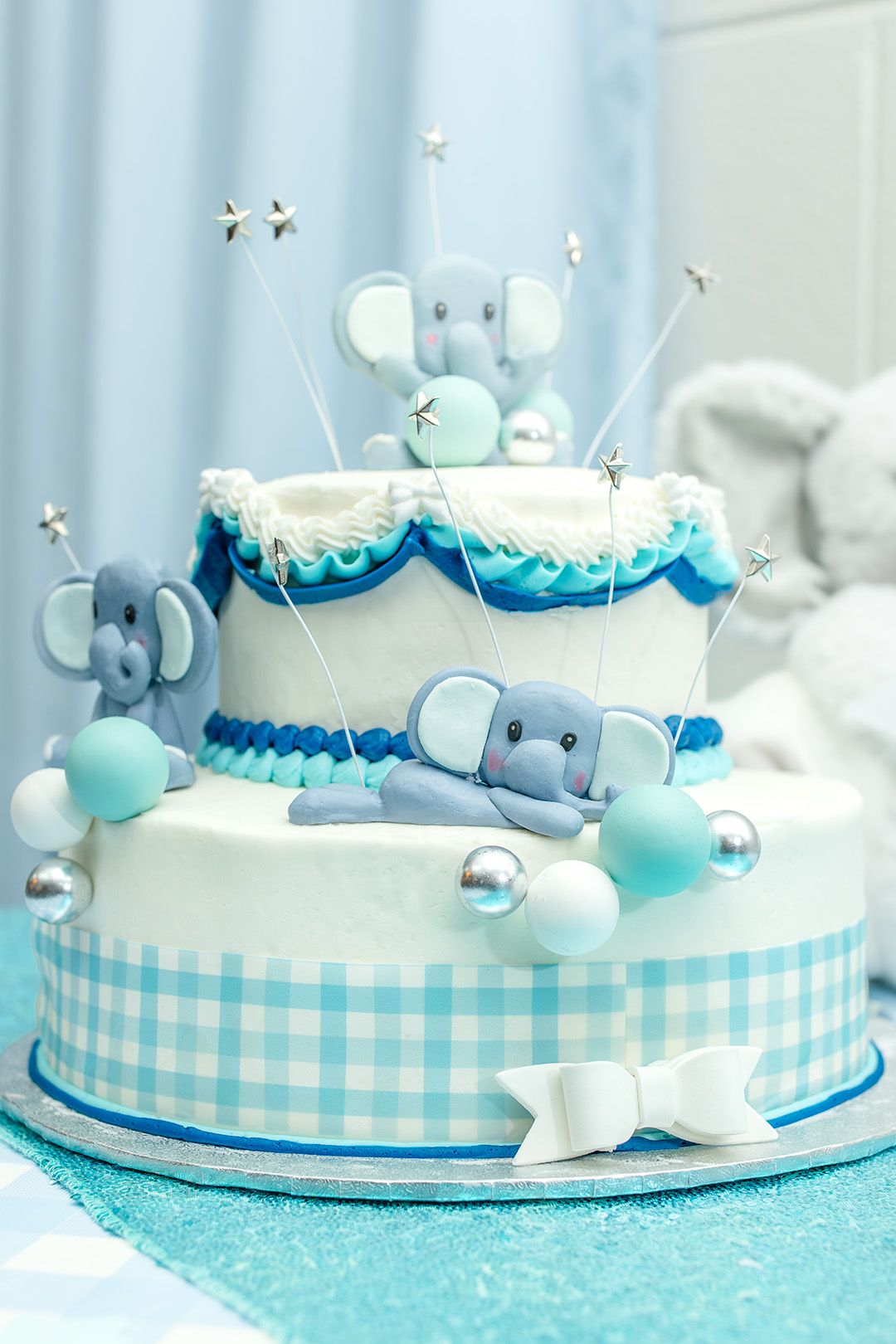 A blue and white themed baby shower cake decorated with cute whale designs and gingham ribbon around the base.
