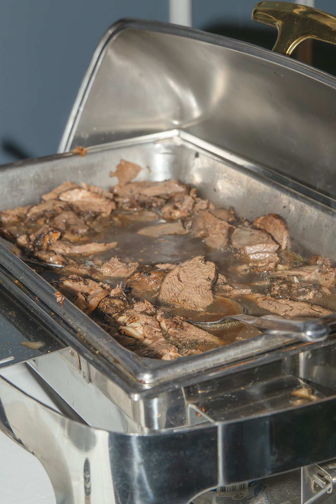 Sliced roast beef in savory juices served in a stainless steel chafing dish at a catered buffet event.