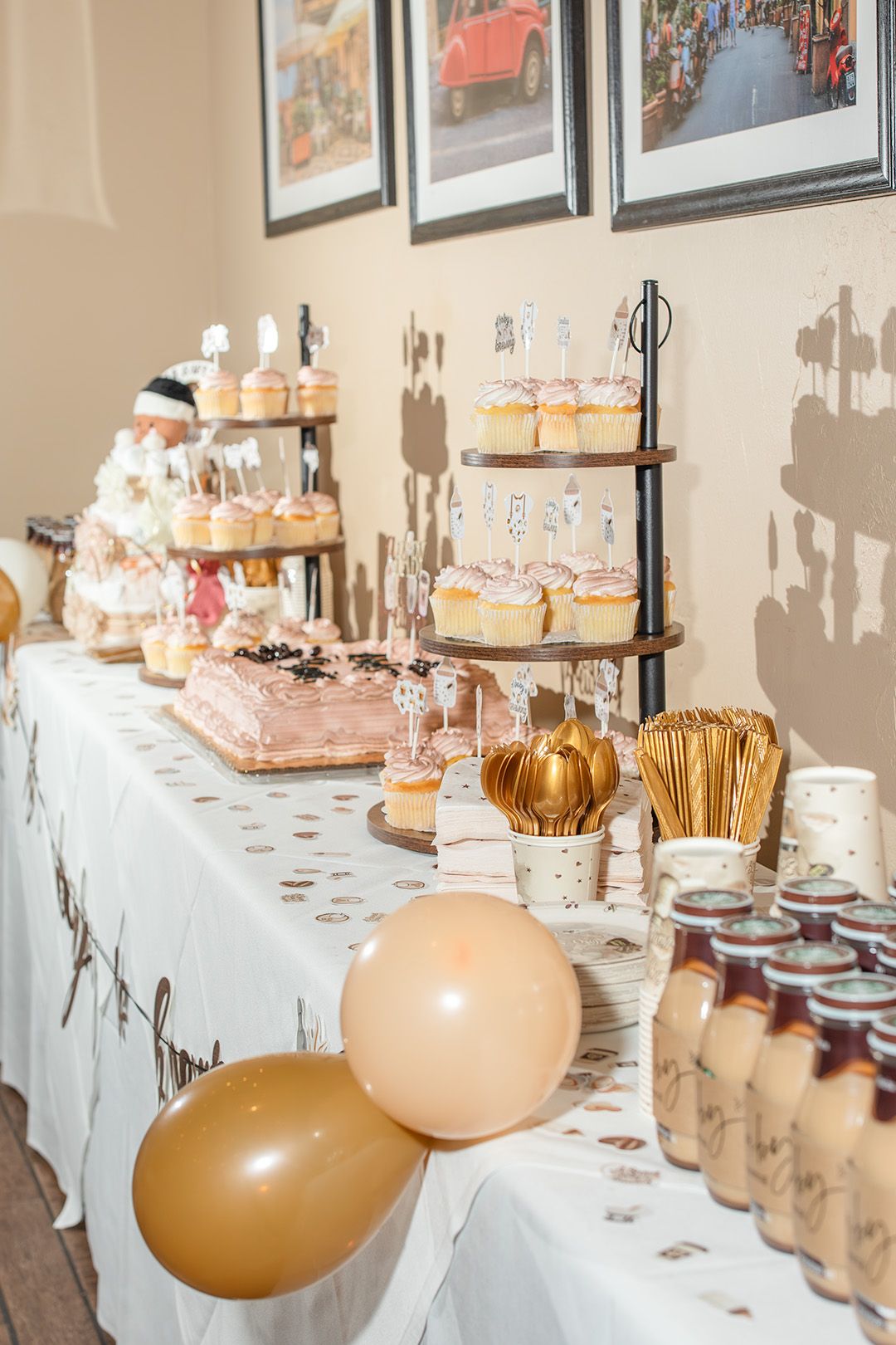 Elegant baby shower dessert table with cupcakes, pink cake, balloons, and sweet treats on white tablecloth.