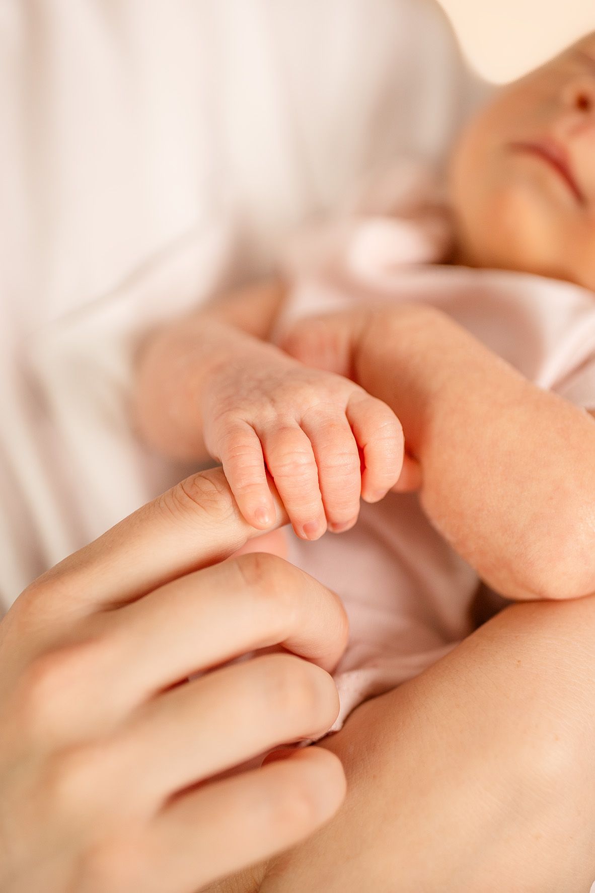 Close-up of a sleeping newborn baby gently gripping an adult's finger, symbolizing love and parental bond.