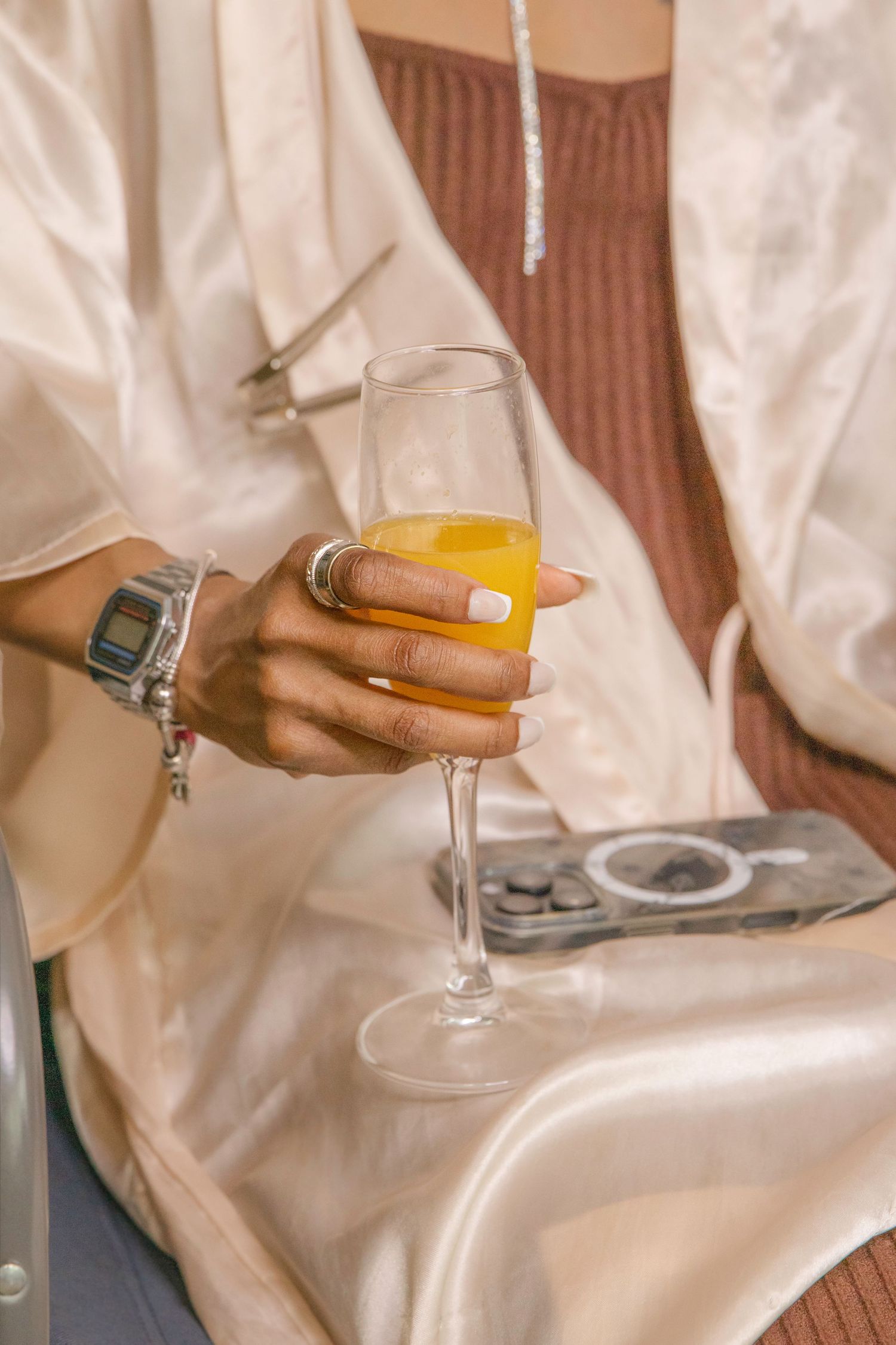 Person in white holding a champagne glass against a light-colored fabric background.