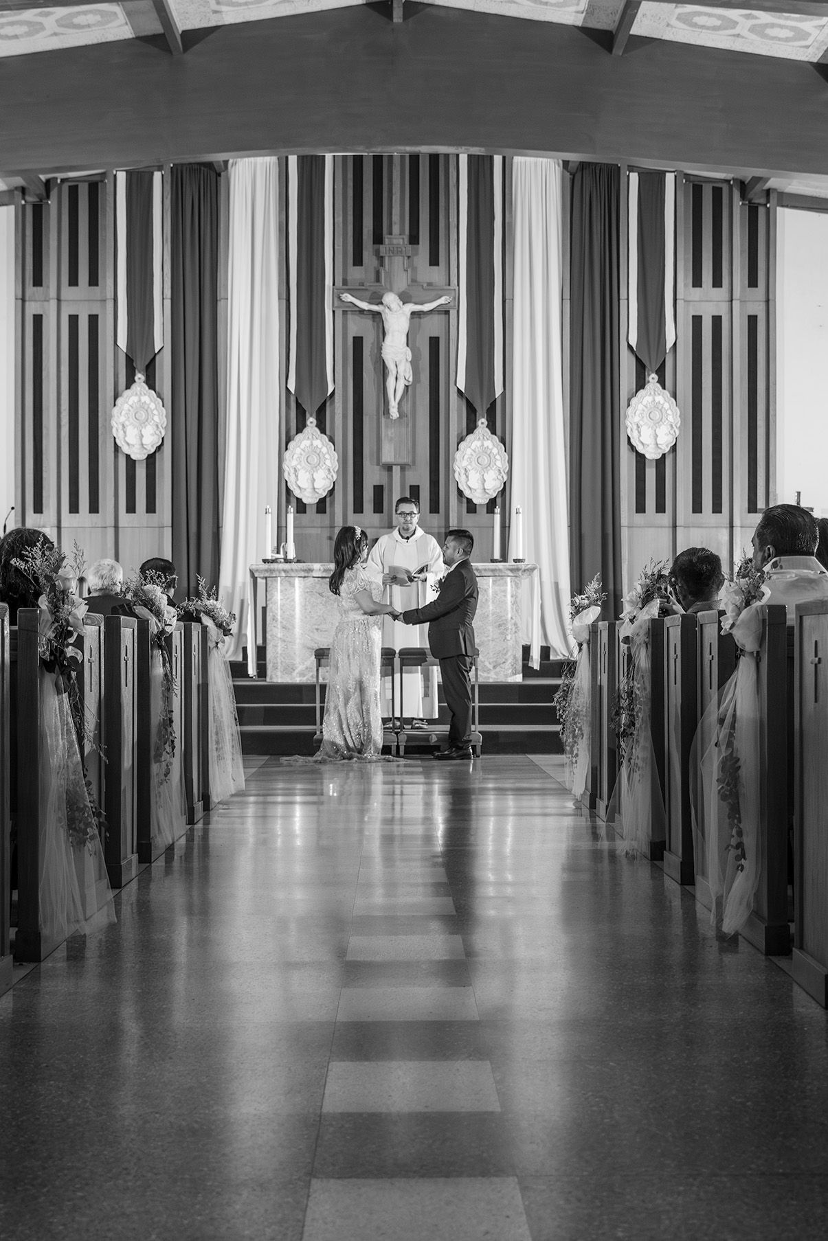 Black and white photo of a couple exchanging vows at a church altar during a wedding ceremony.