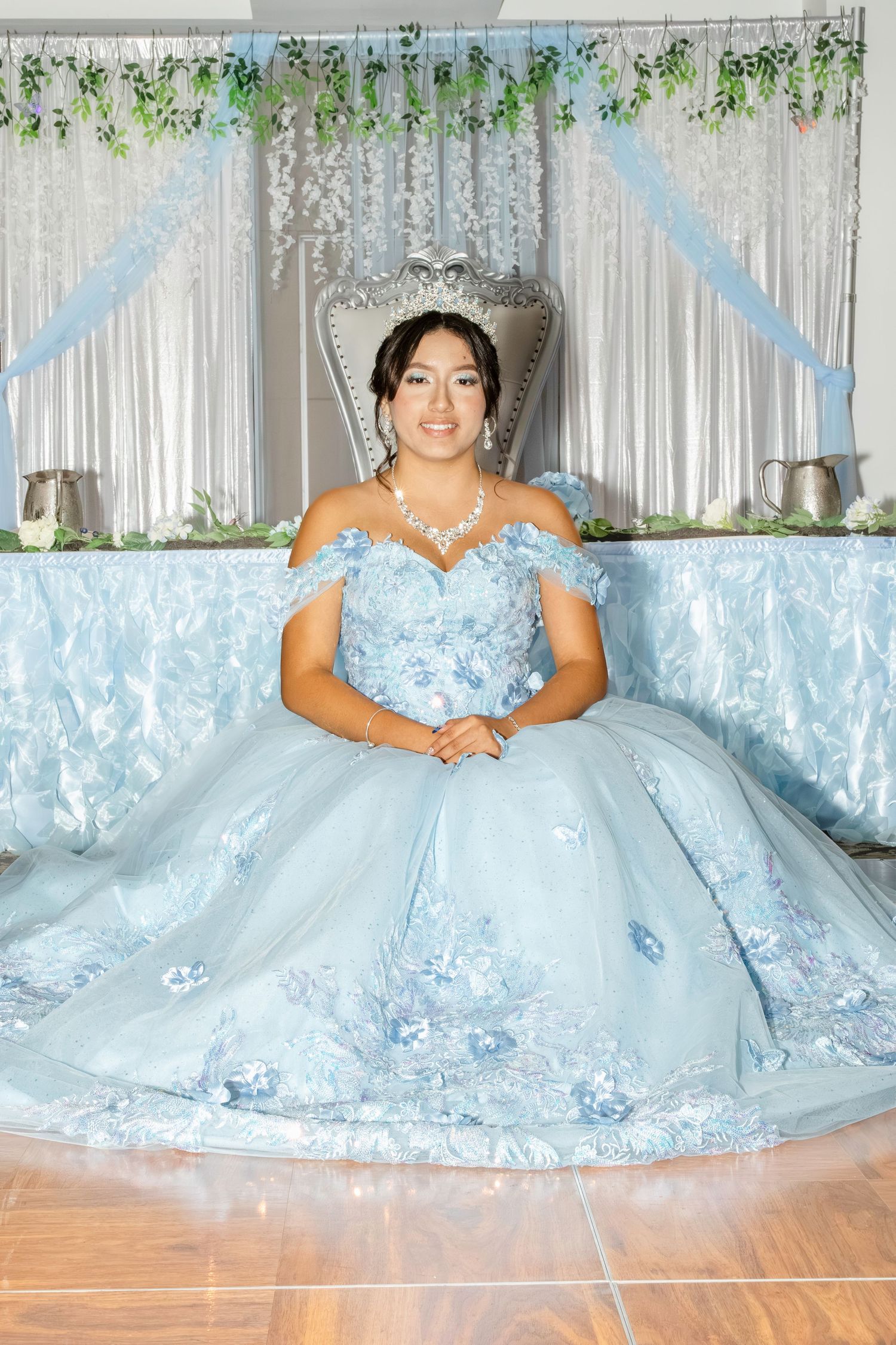 A light blue quinceañera gown with intricate beading and floral details is showcased in five elegant poses on a wooden floor.