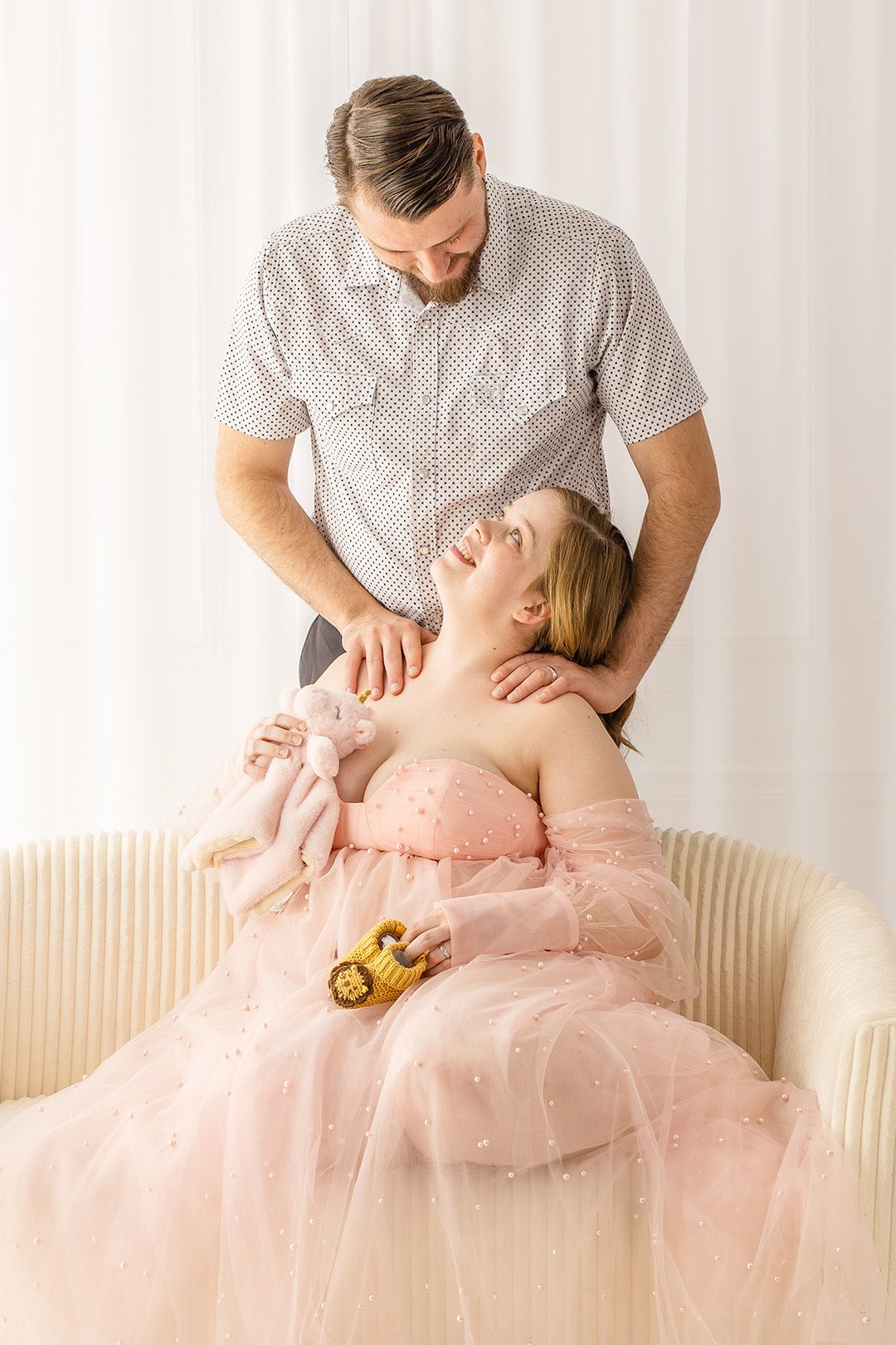 A tender moment captured between a couple in a bright room with a flowing pink tulle dress.