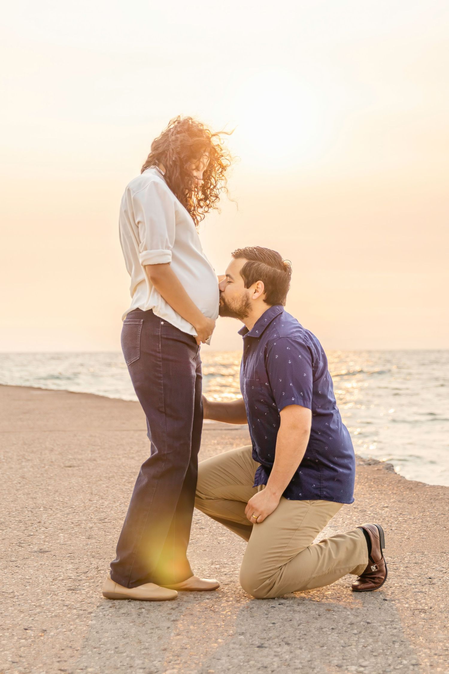 A tender moment between a pregnant woman and her partner on the beach at sunset with golden sunlight.