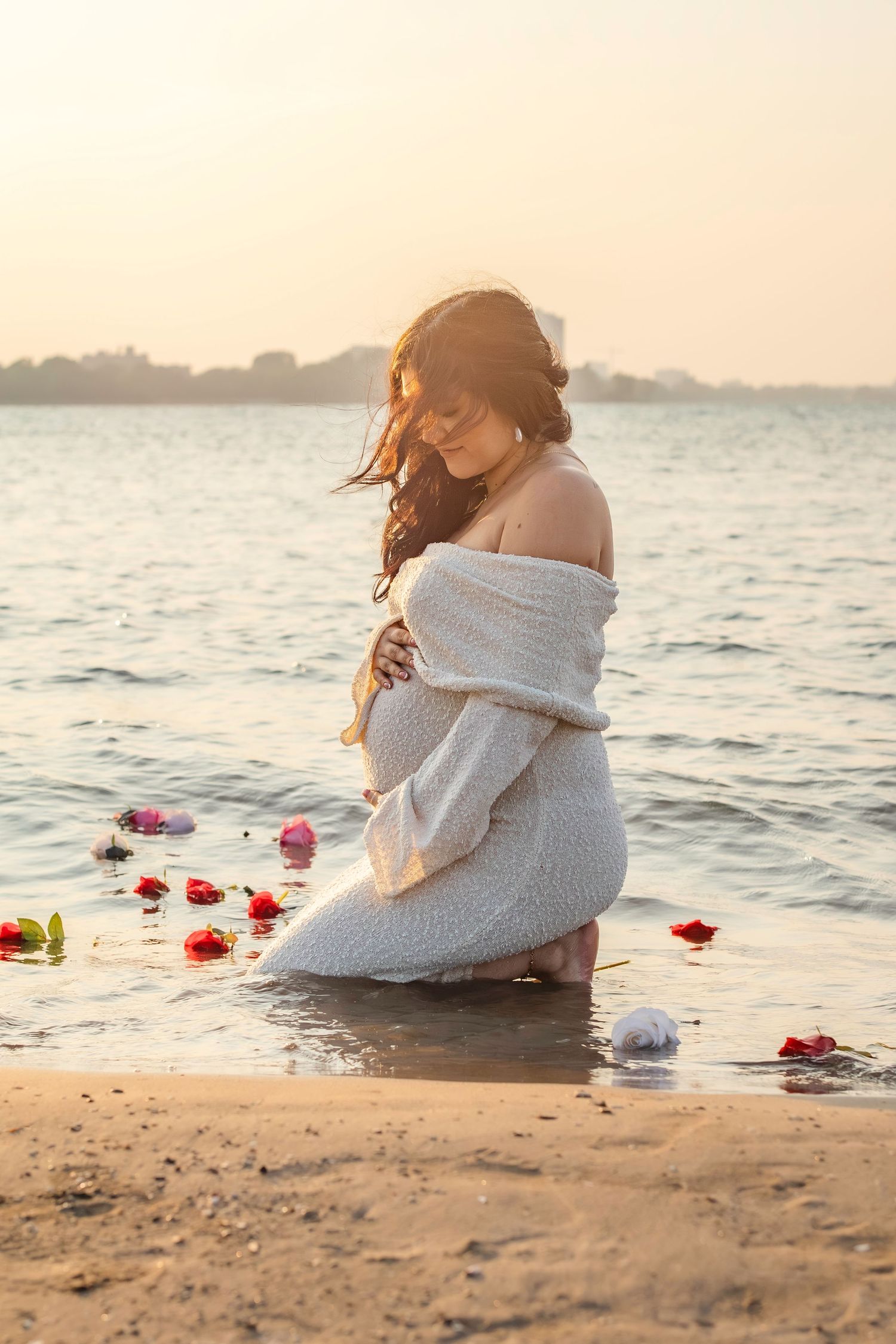 Couple sits embracing on sunset beach with scattered rose petals in romantic seaside setting.