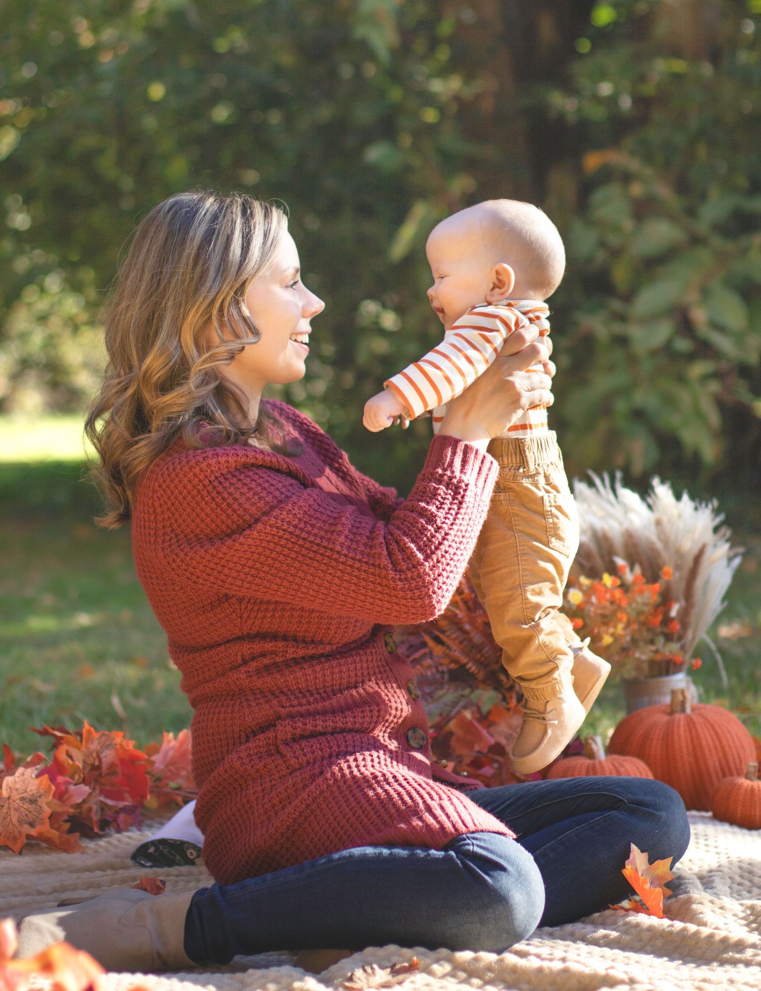 Autumn family photoshoot with two people and pumpkins on blanket in outdoor setting.