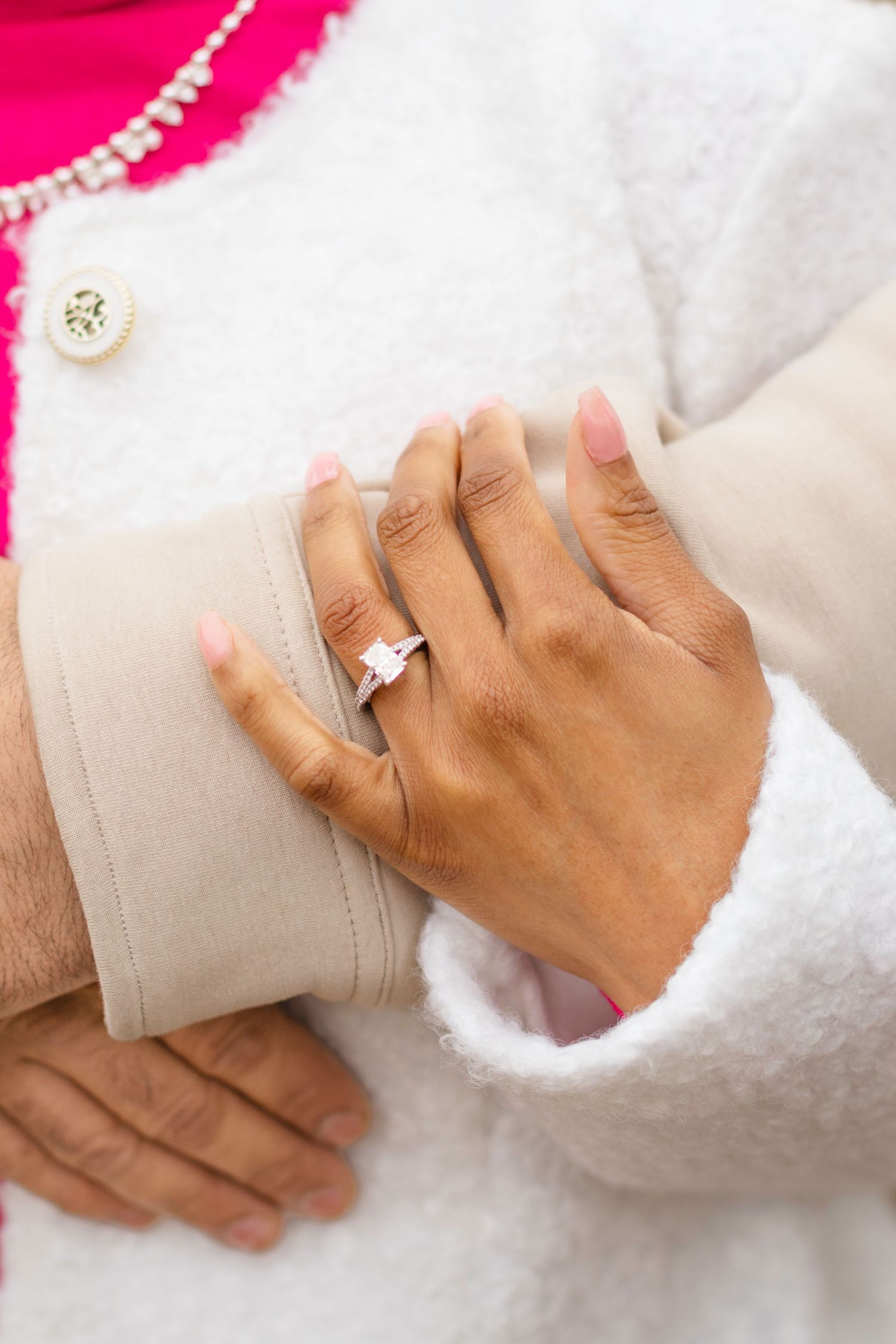 Close-up of hands displaying an engagement ring against white and pink clothing.