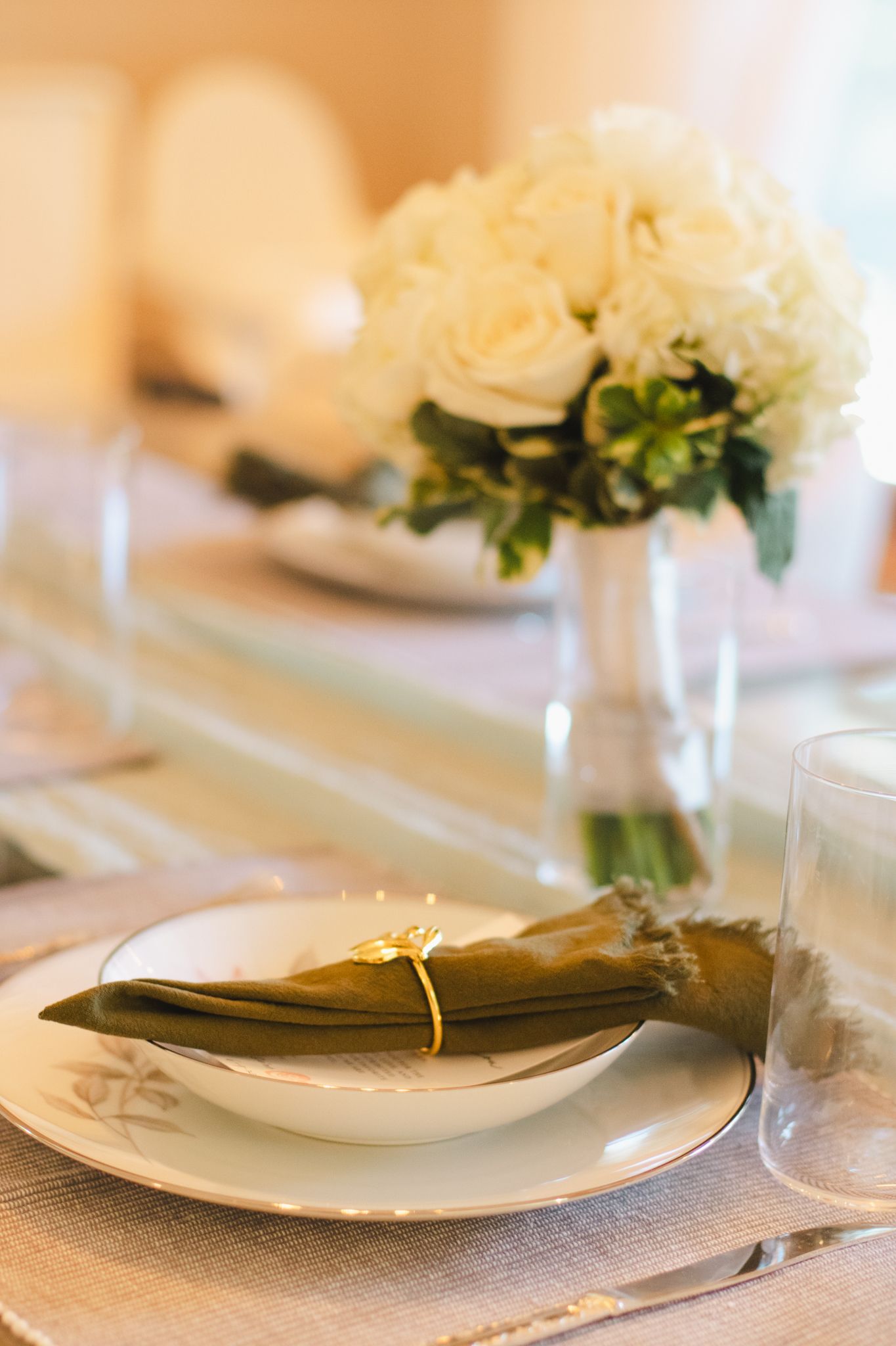 Elegant table setting with white roses and folded napkin on white tablecloth.